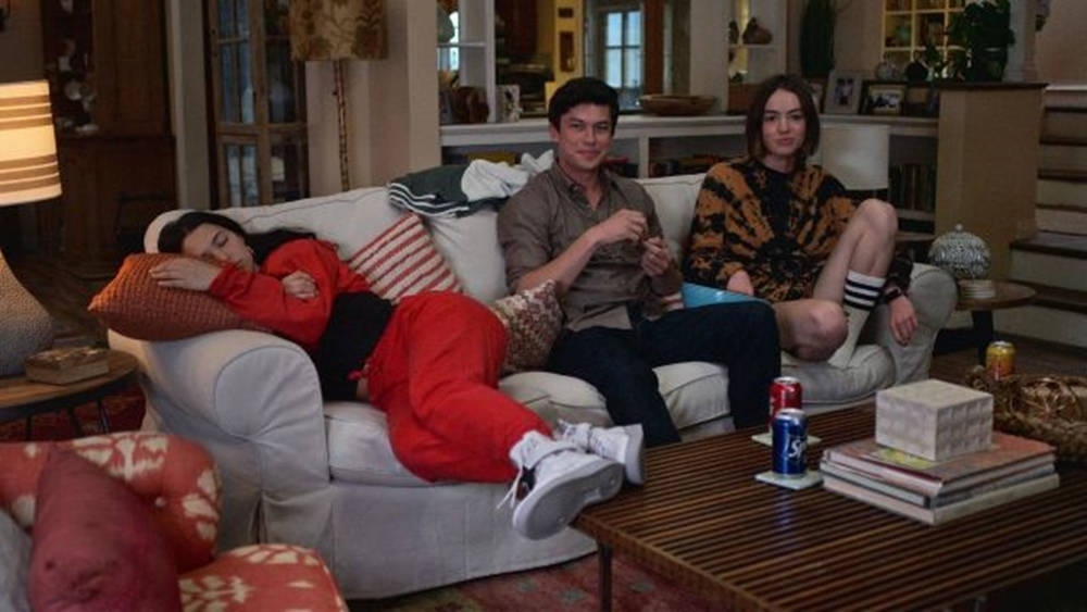 三個青少年在沙發上，一個穿紅色運動服睡覺，其他醒著