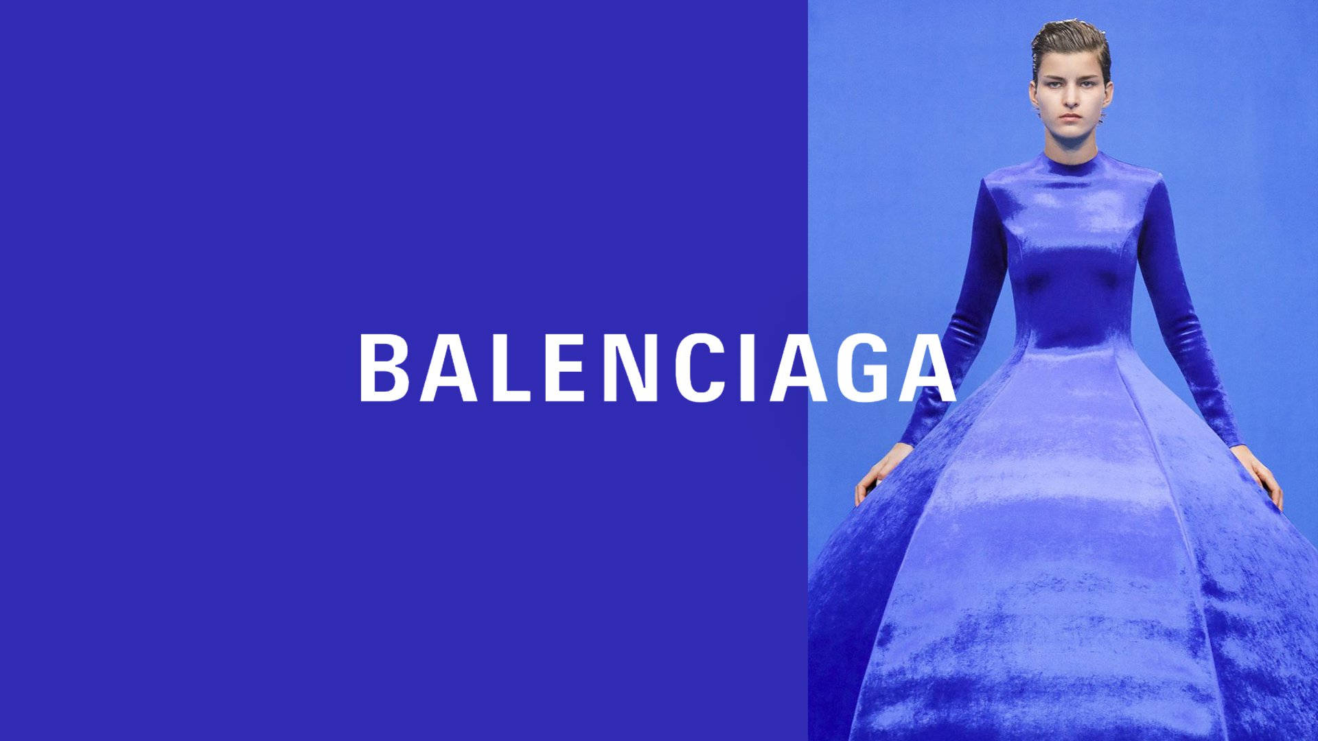 當代 Balenciaga 藍色禮服 壁紙 — 模特兒身穿寬大的皇家藍色長袍，站在帶有 'BALENCIAGA' 文字的藍色分割背景前。