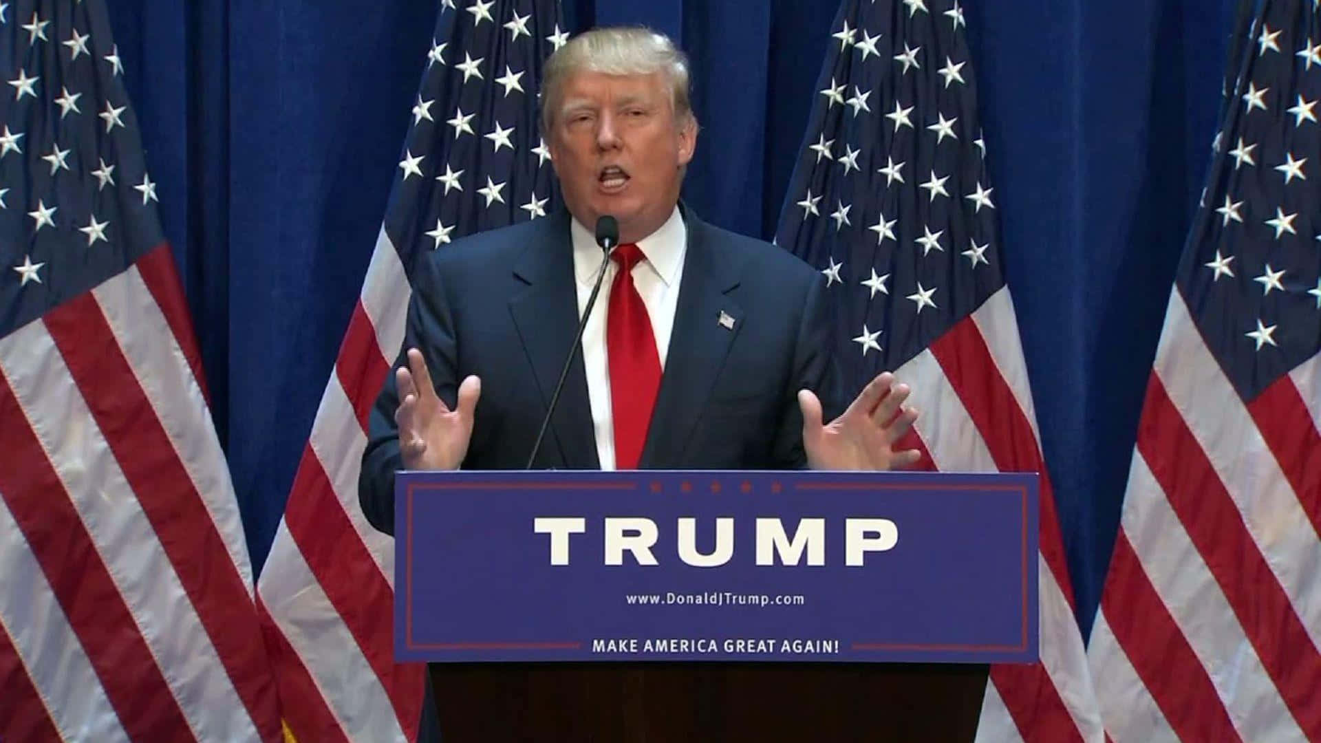 trump 桌布 壁紙 — 當勞·特朗普在講台上發言，講台上有「TRUMP」和「MAKE AMERICA GREAT AGAIN」字樣，兩側有美國國旗。
