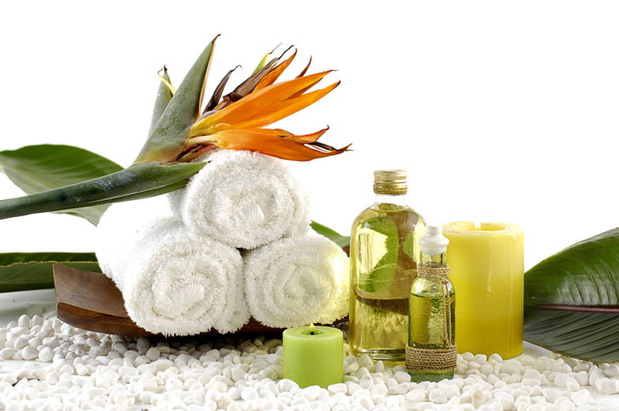 Ayurveda HD 桌布 壁紙 — 疊起的白色毛巾和熱帶花卉放在白色卵石上，旁邊有蠟燭和油瓶，營造寧靜的水療場景。