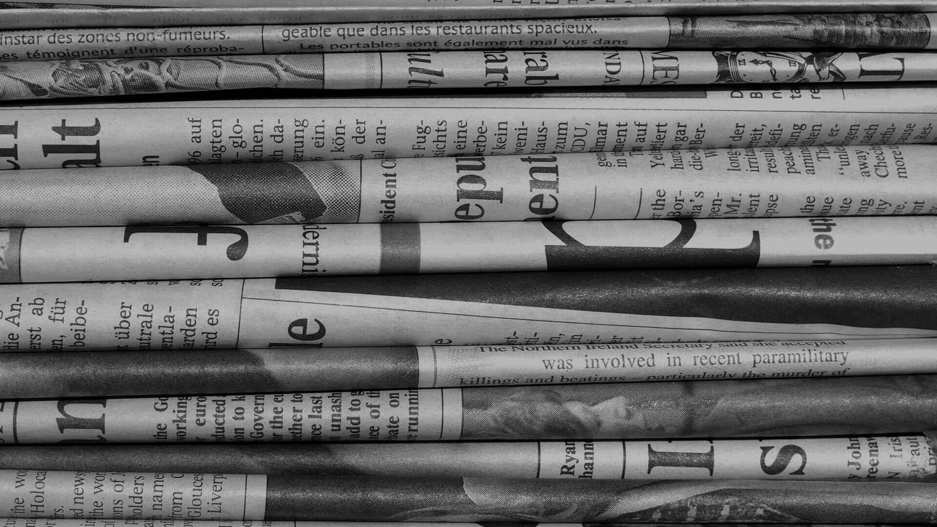 Black And White Newspaper 桌布 壁紙 — 疊起的黑白報紙，帶有粗體標題和褪色文字，營造出有紋理的復古新聞檔案。