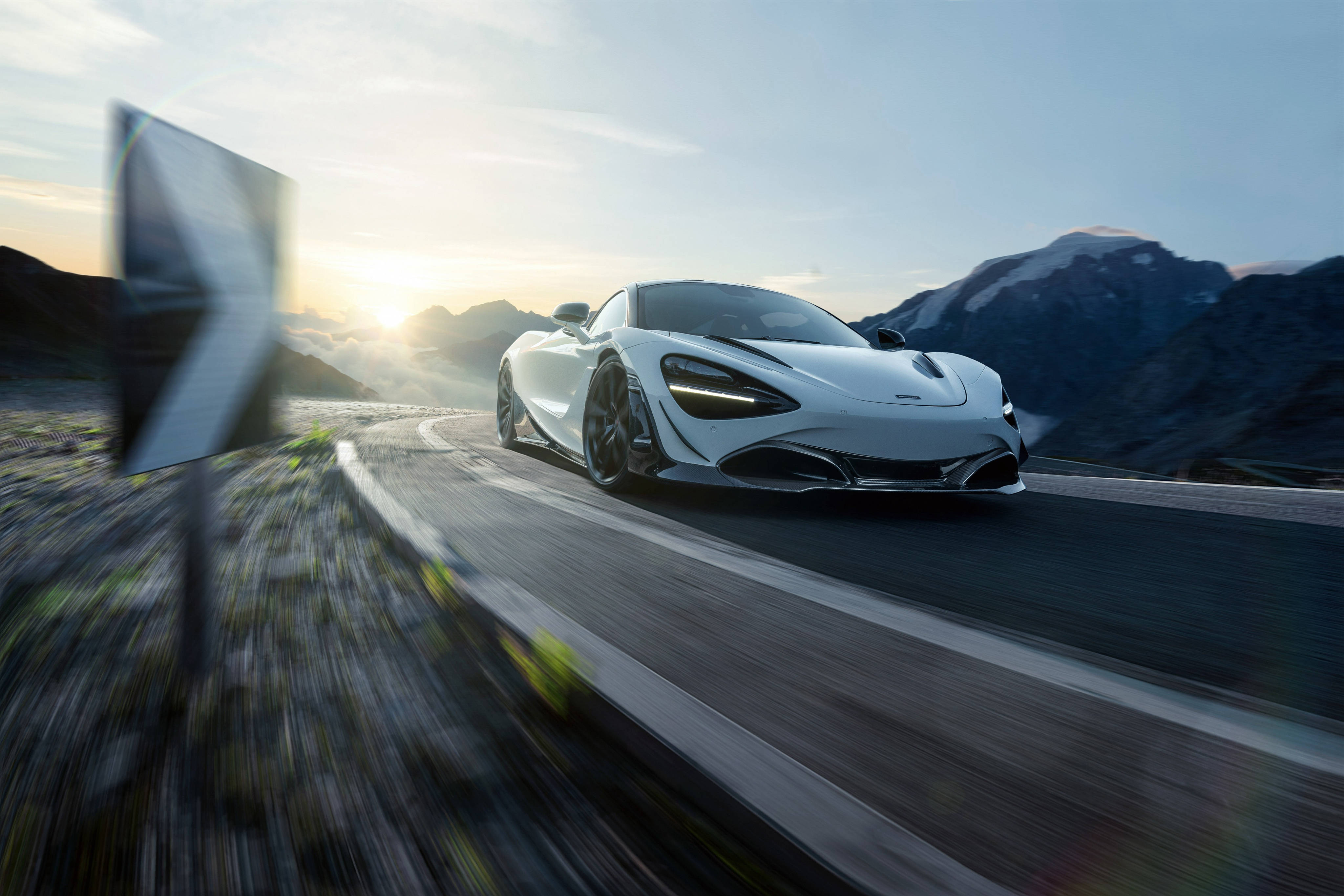 疾馳中的白色麥拉倫720S 壁紙 — 一輛時尚的白色跑車在日出時沿著蜿蜒的山路疾馳，背景是白雪覆蓋的山峰，帶有模糊的動感效果。