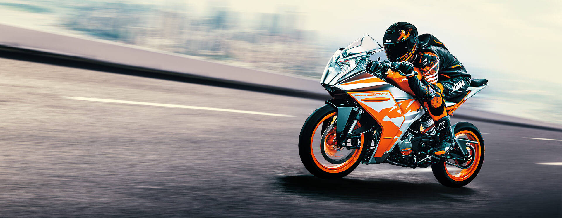 疾馳的KTM RC 200 壁紙 — 一名騎士在鮮豔的橙色和白色KTM運動電單車上傾斜入彎，在模糊的高速公路上飛馳。