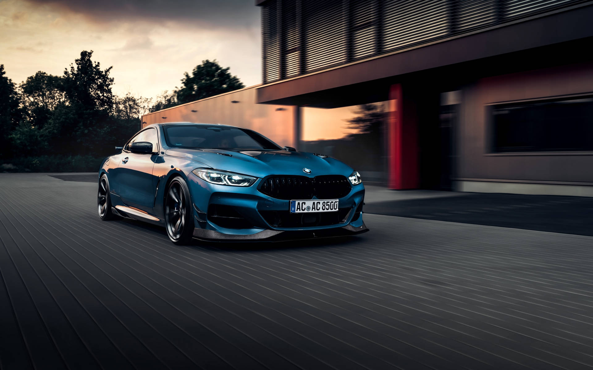 藍色BMW M8 Coupe在黃昏時高速駛過現代建築。