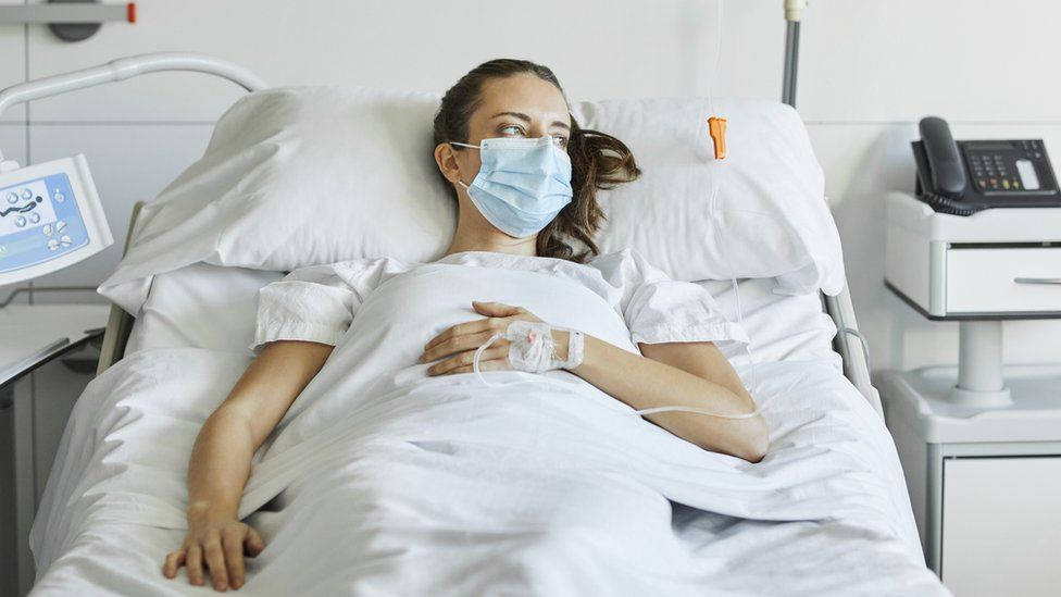 醫院床上戴著口罩和接受輸液的女性