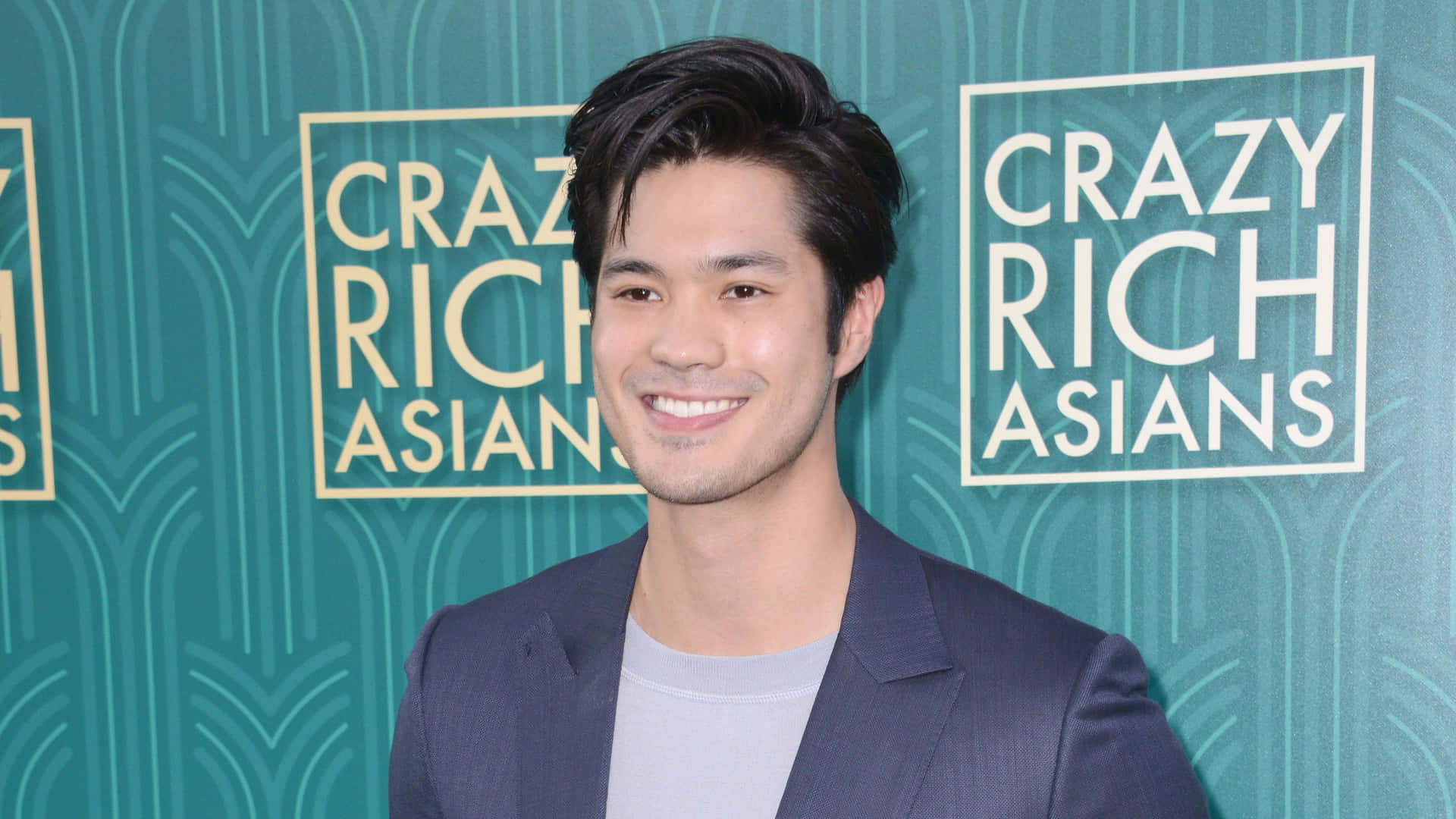身穿西裝的男子在 'Crazy Rich Asians' 背景的活動中微笑。
