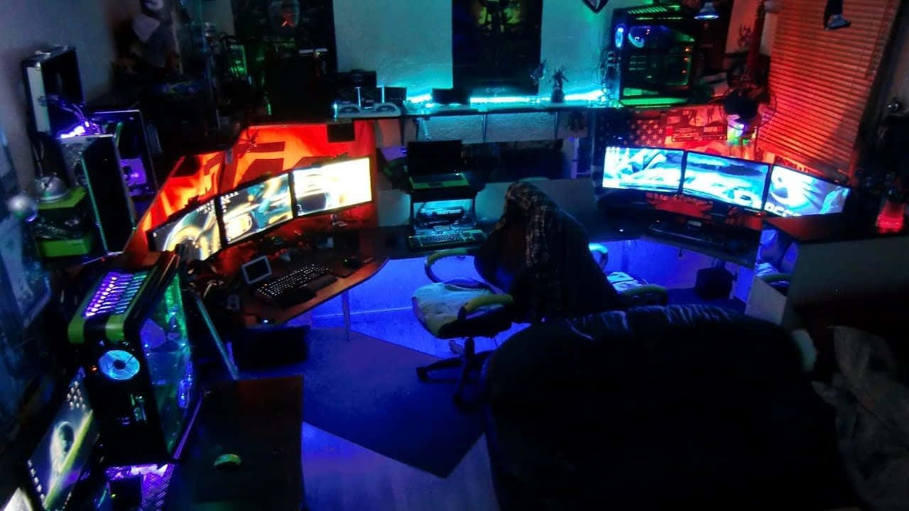 瘋狂遊戲洞穴設置圖片 壁紙 — 一位遊戲玩家坐在昏暗的房間中，被多個顯示器和自訂電腦機箱發出的霓虹藍光和紅光所籠罩。