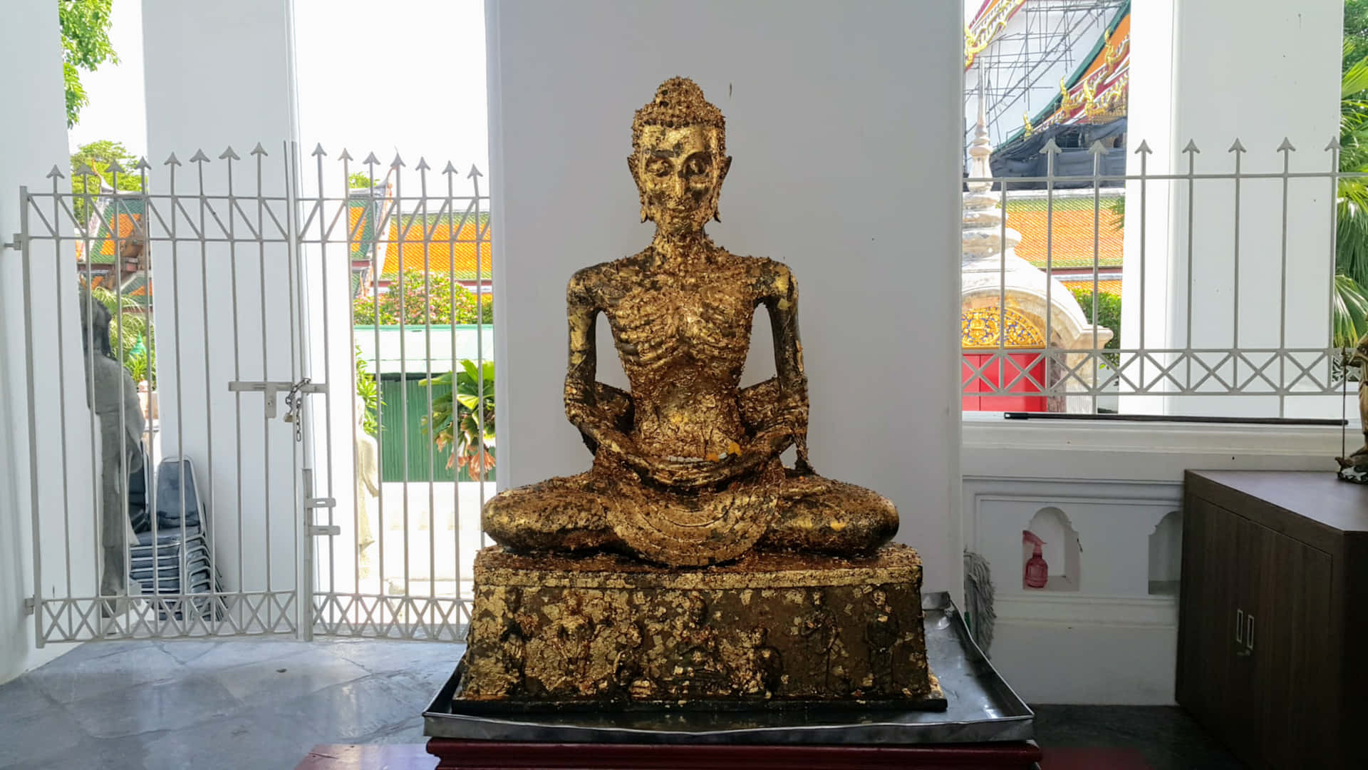 寺廟內部的金色佛像，白色柱子和外面的綠植。