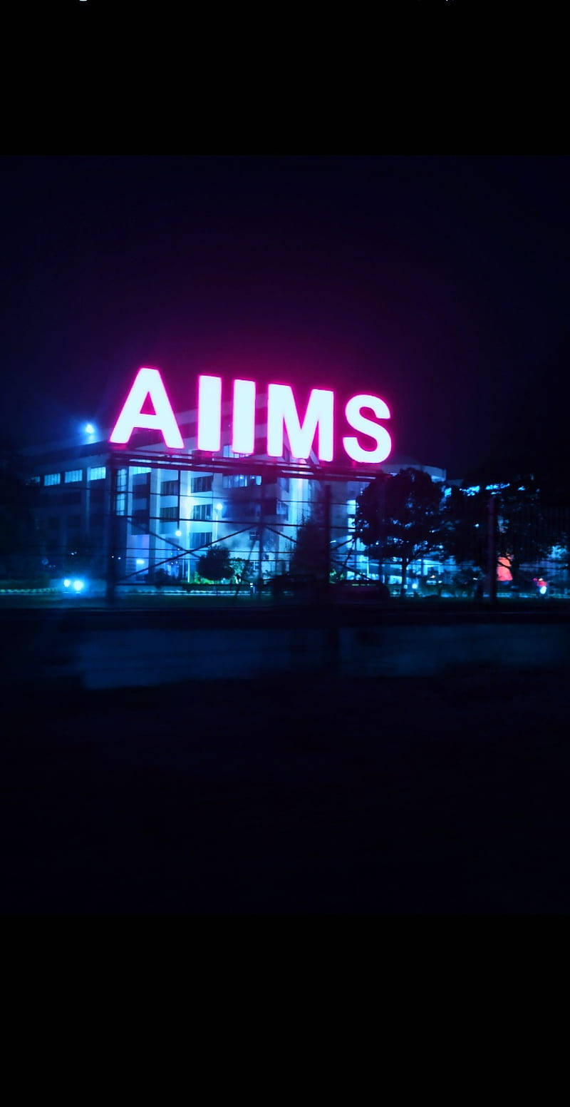AIIMS建築的夜景，帶有發光的粉紅色標誌和反射在潮濕地面上的藍色燈光。