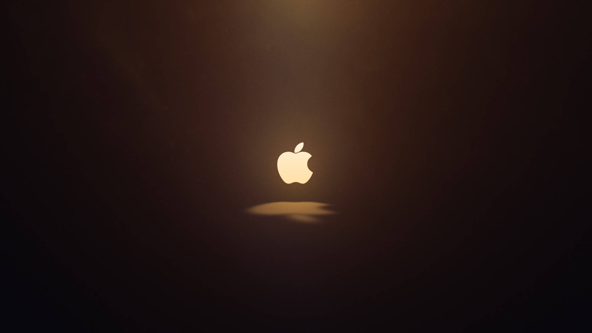 發光的Apple標誌在黑暗空間中置中，帶有柔和光線。 — 蘋果 壁紙
