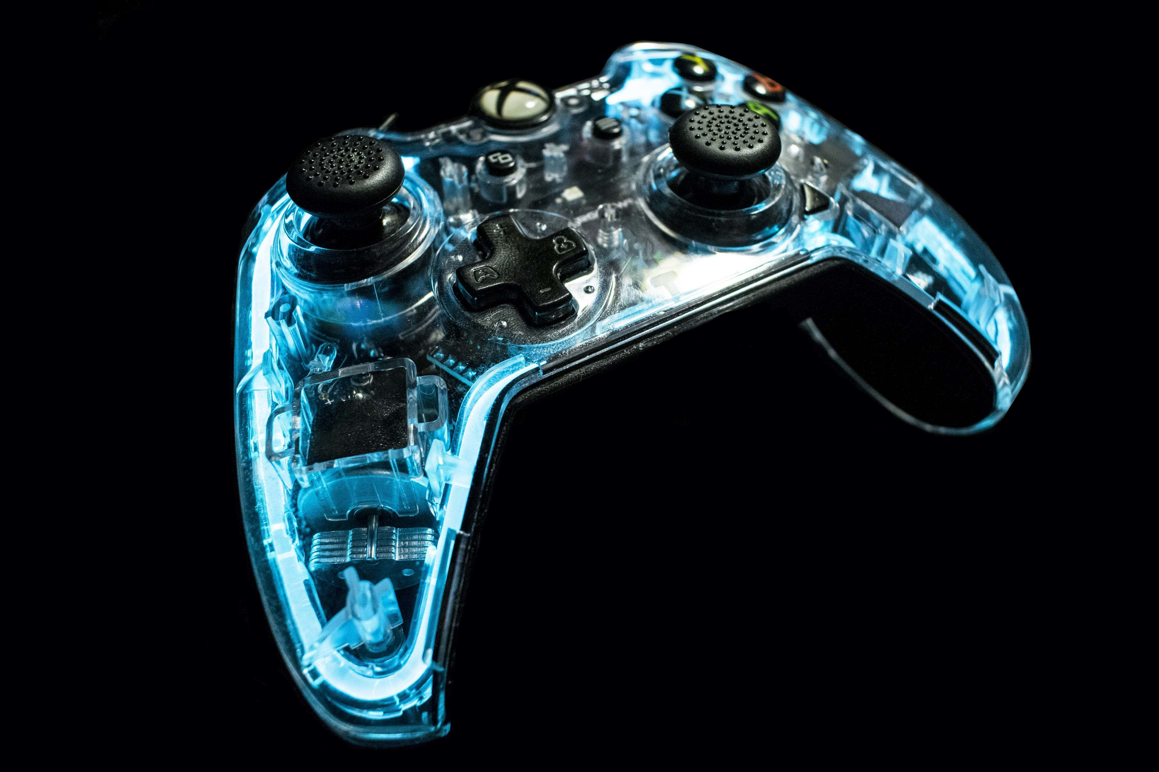 發光 LED 遙控遊戲控制器 壁紙 — 一個半透明的藍色Xbox控制器在黑色背景上發光，揭示內部電路和組件。