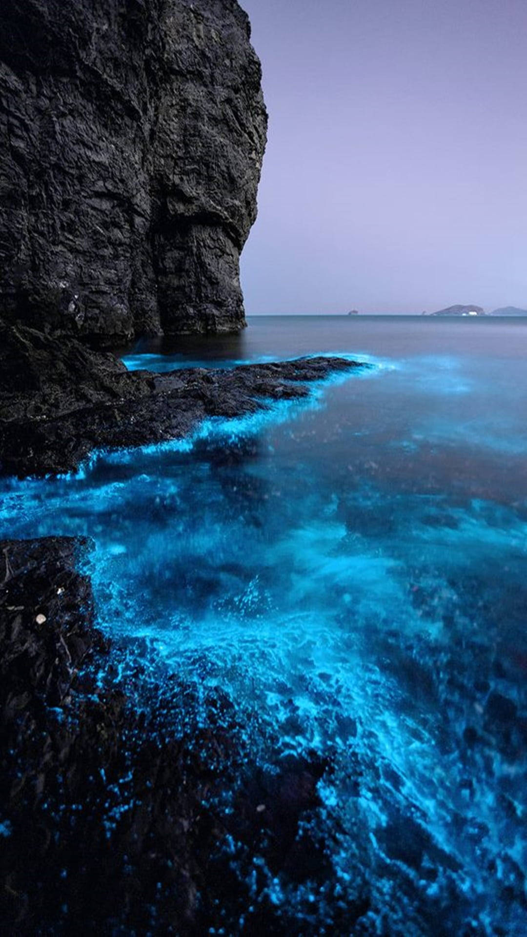 發光海水 壁紙 — 在暮色天空下，發光的藍綠色生物發光波浪拍打著黑暗的火山懸崖。