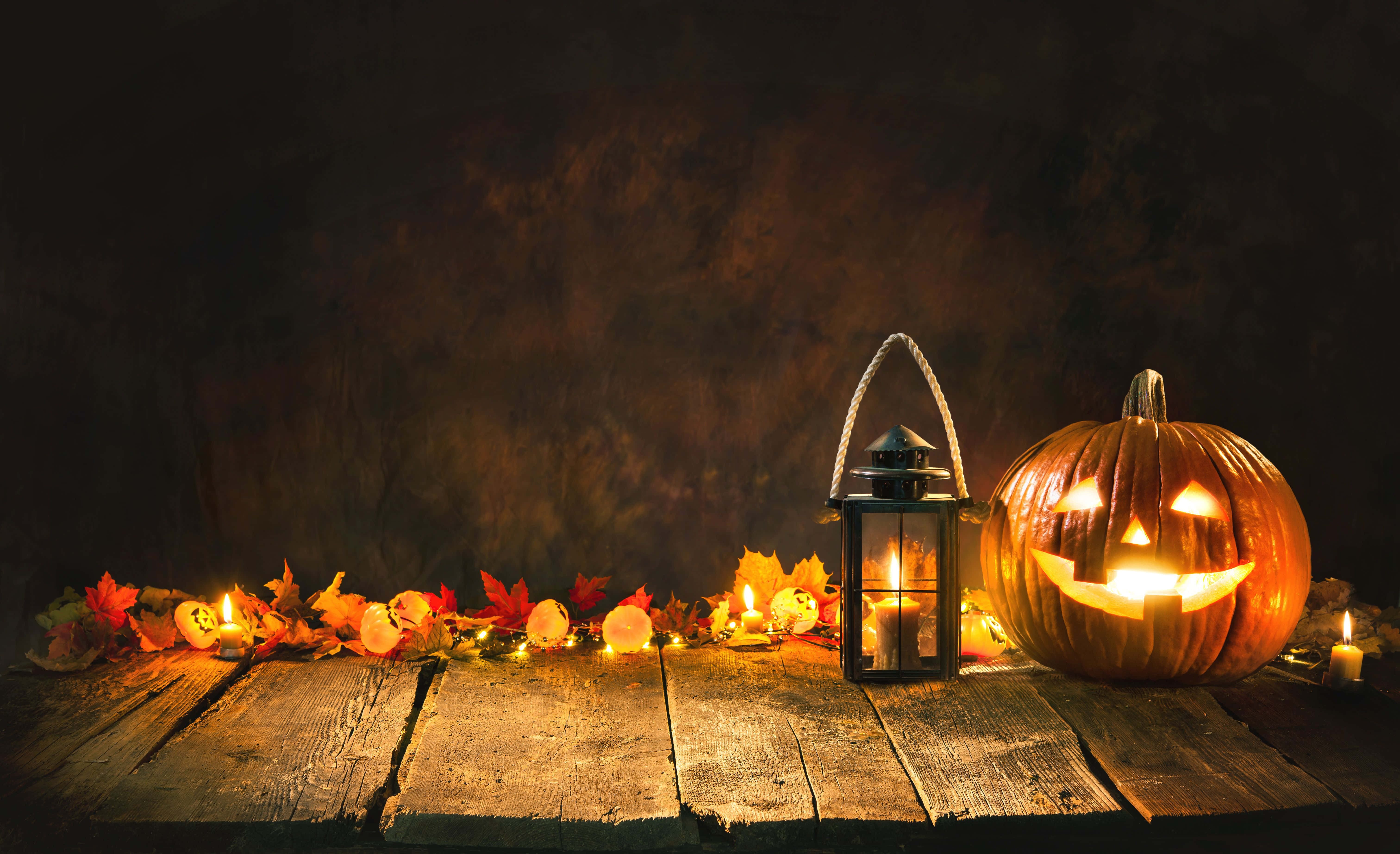 Halloween Props 桌布 壁紙 — 發光的傑克南瓜燈和燈籠將溫暖的光線投射在鄉村木桌上的秋葉和蠟燭上。