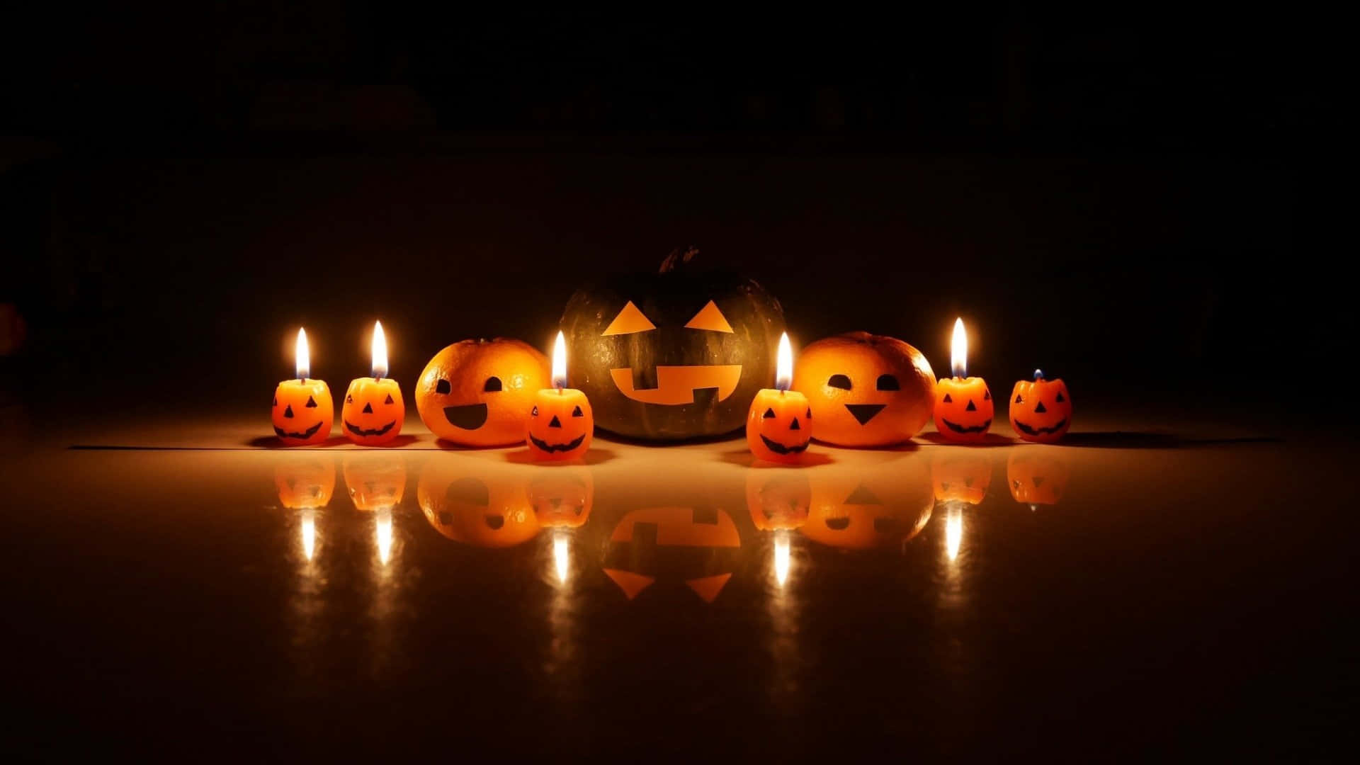 Halloween Candles 桌布 壁紙 — 發光的傑克南瓜燈和蠟燭在黑暗的光滑表面上投射出溫暖的橙色反射，營造出詭異的萬聖節場景。