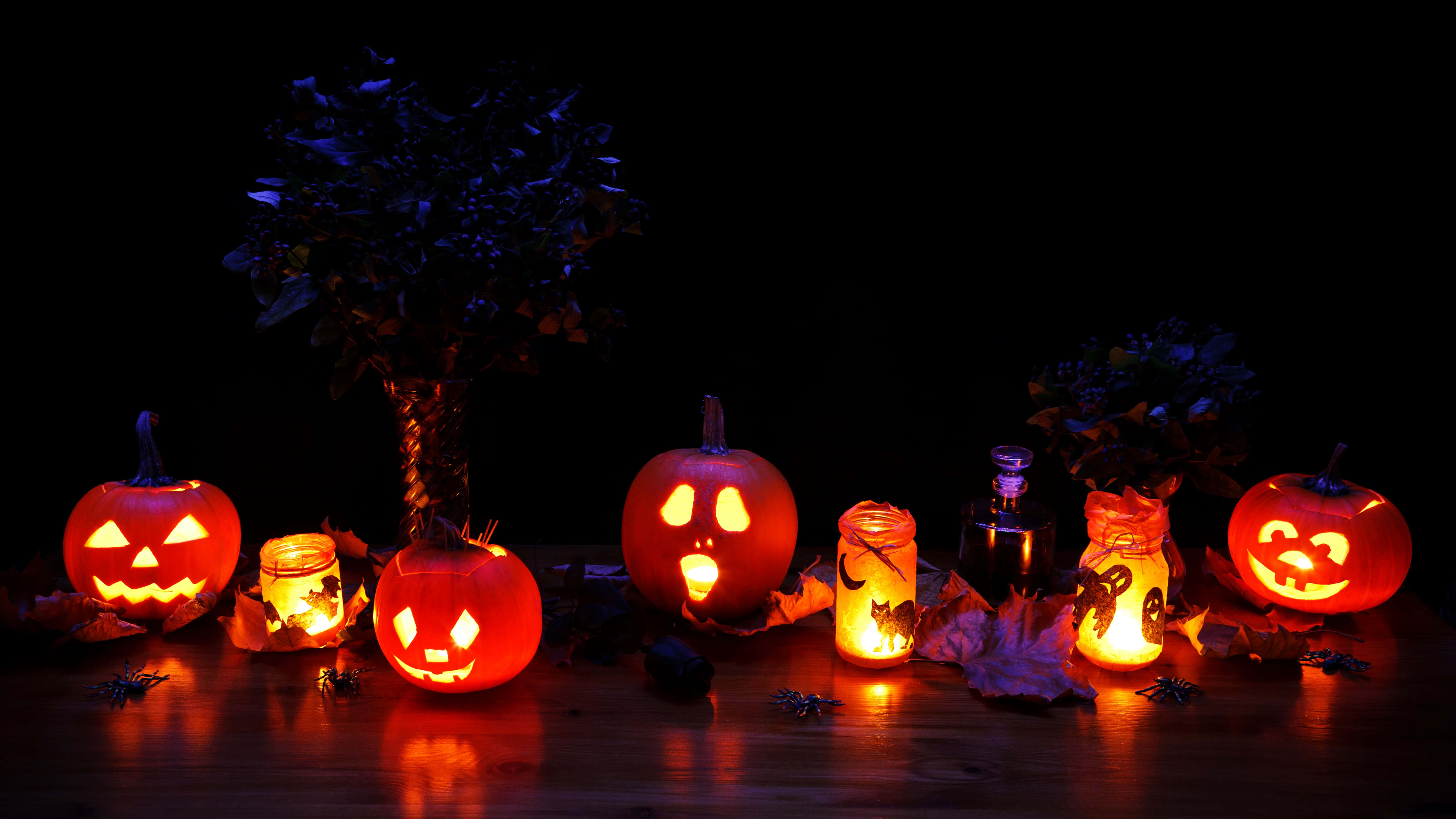Halloween Props 桌布 壁紙 — 發光的傑克南瓜燈和蠟燭罐在黑暗背景下，在木桌上投射出詭異的橙色光芒。