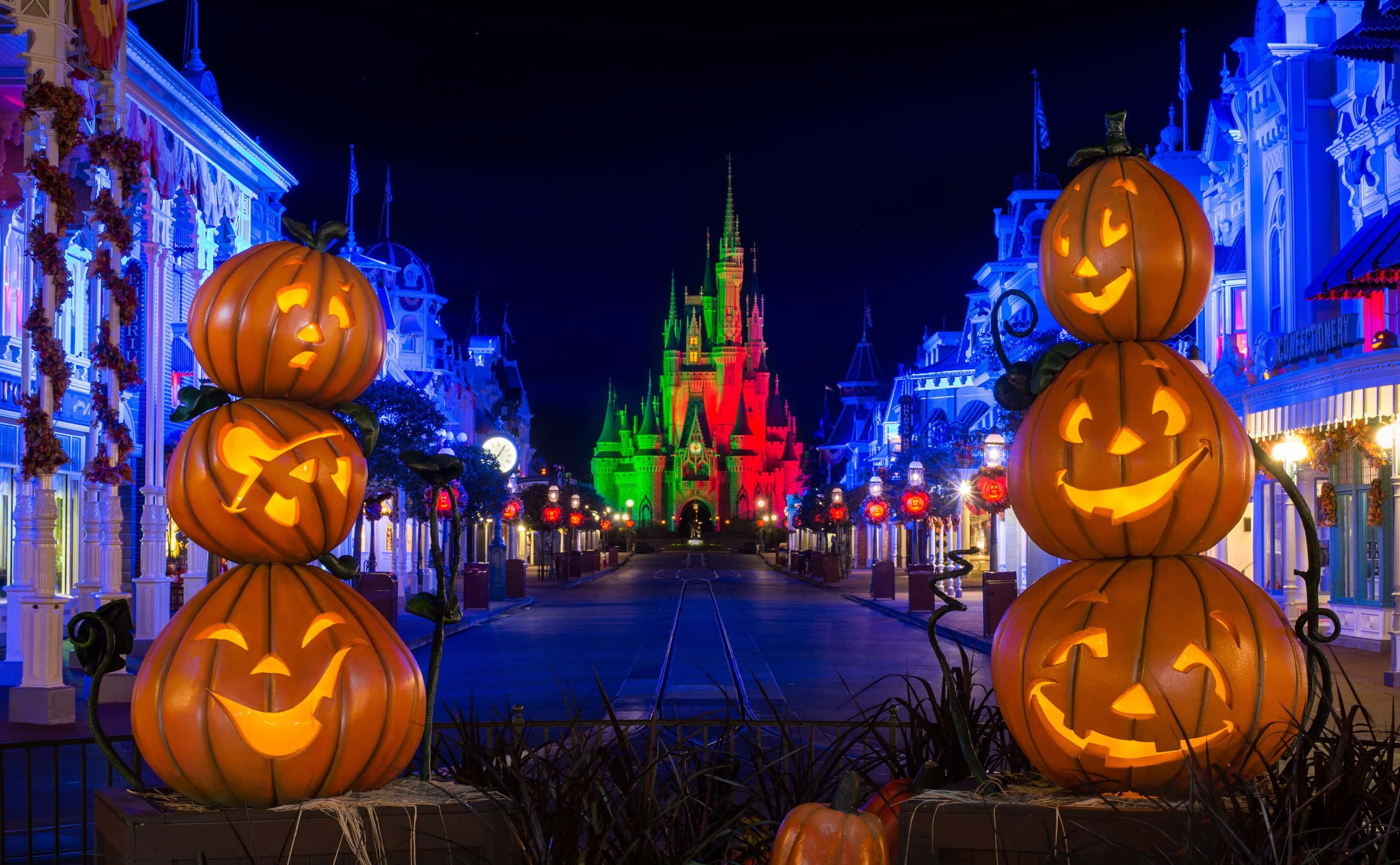Disney Halloween 桌布 壁紙 — 發光的南瓜堆排列在通往燈火通明城堡的節日夜晚街道兩旁。