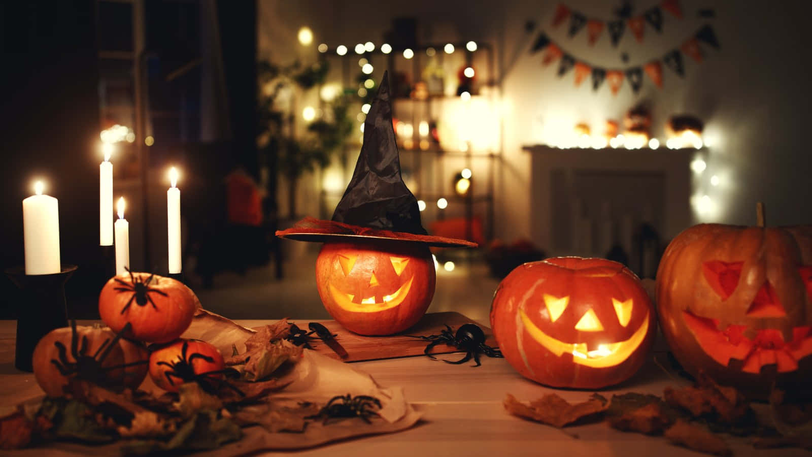 Halloween Candles 桌布 壁紙 — 發光的南瓜配上女巫帽和蠟燭，在裝飾著蜘蛛和秋葉的萬聖節餐桌上投射出溫暖的光芒。