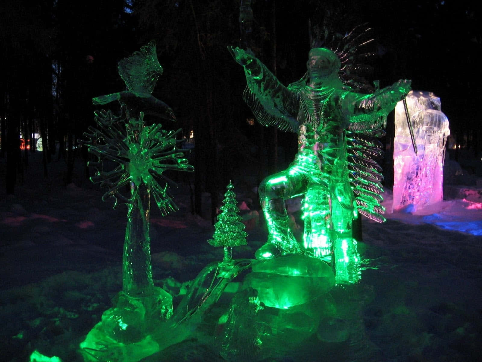 Ice Sculpture 桌布 壁紙 — 發光的綠色冰雕，描繪一個坐著的人物和樹木，在夜晚黑暗的雪森林中閃耀。