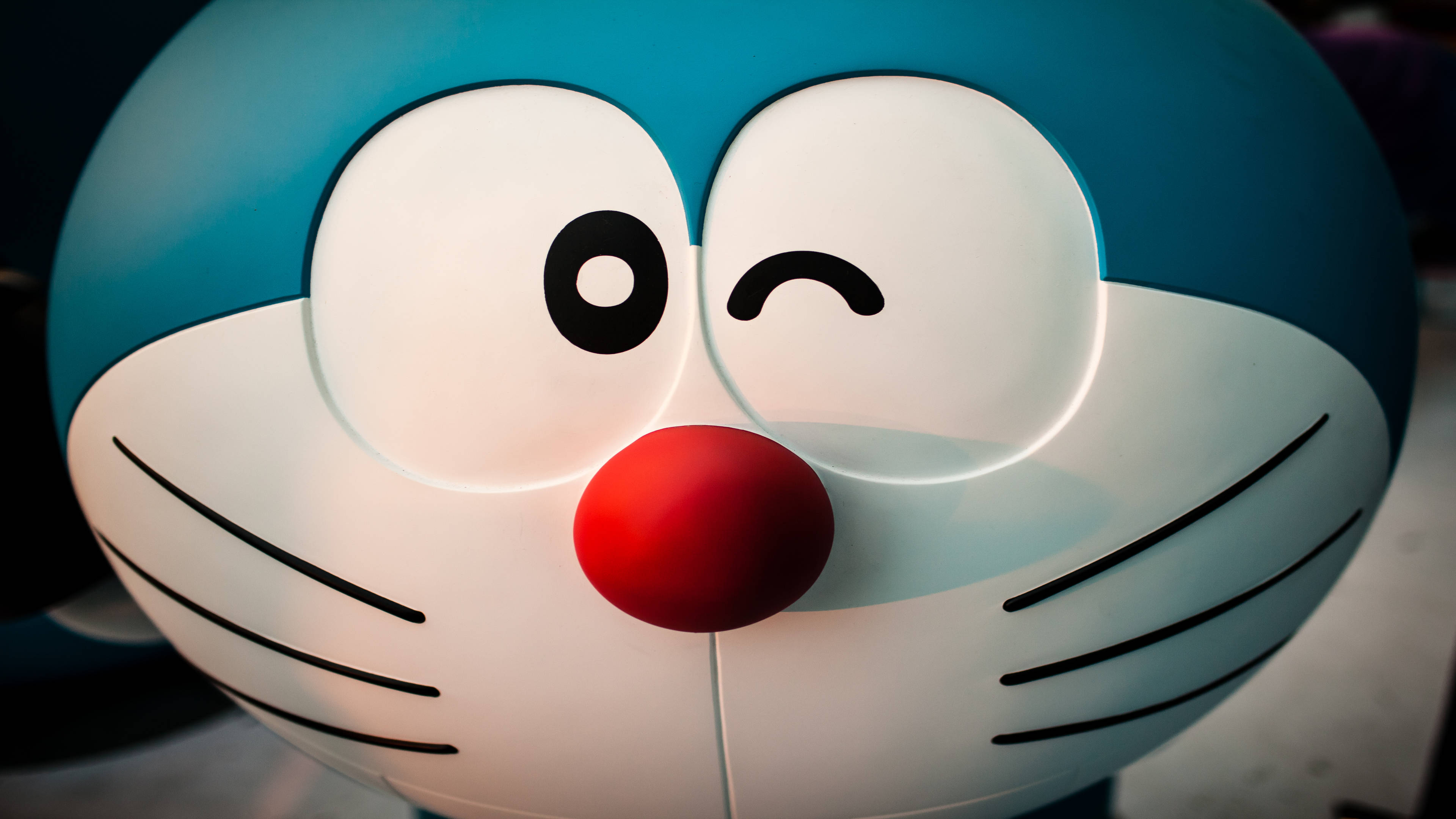 Doraemon 桌布 壁紙 — 發光藍色機械貓的特寫，有一隻眼睛在眨眼，紅色的鼻子。