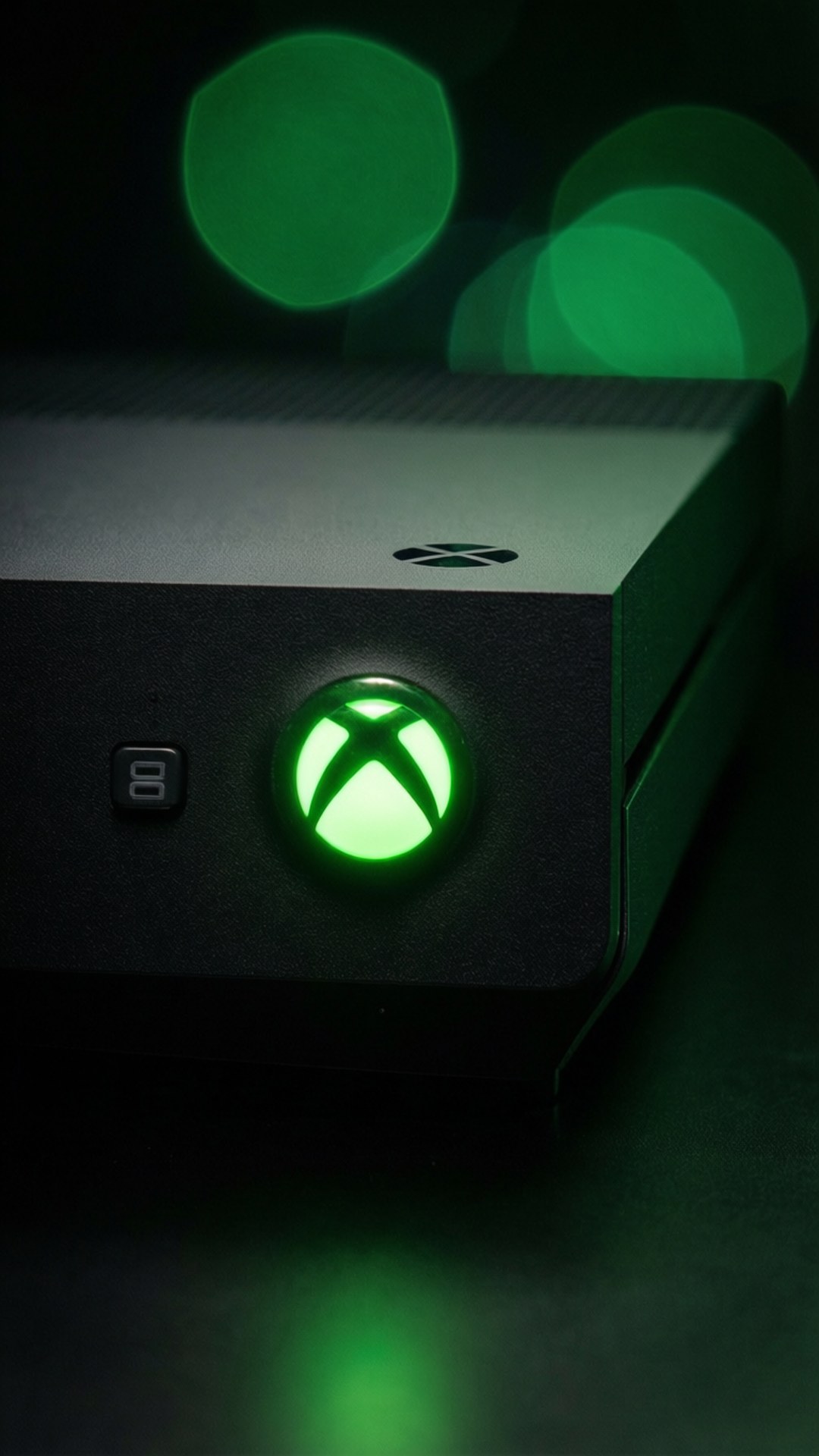 發光電源按鈕特寫 壁紙 — 黑色Xbox主機特寫，在帶有綠色散景的黑暗背景下散發出鮮豔的綠色光芒。