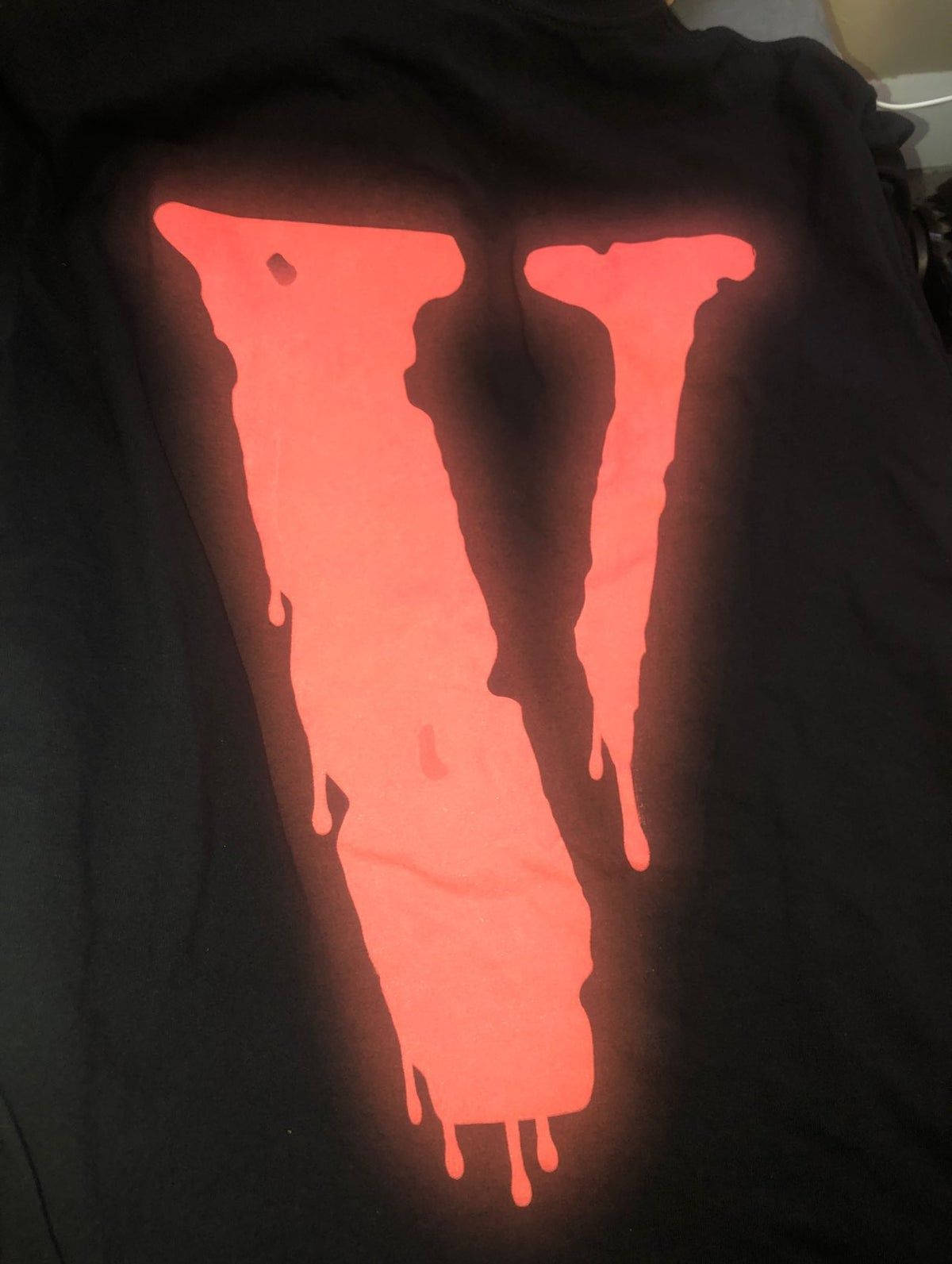 發光黏液 VLONE 標誌 壁紙 — 一件黑色T恤在深色背景上展示了一個發光的橙色滴落「V」標誌。