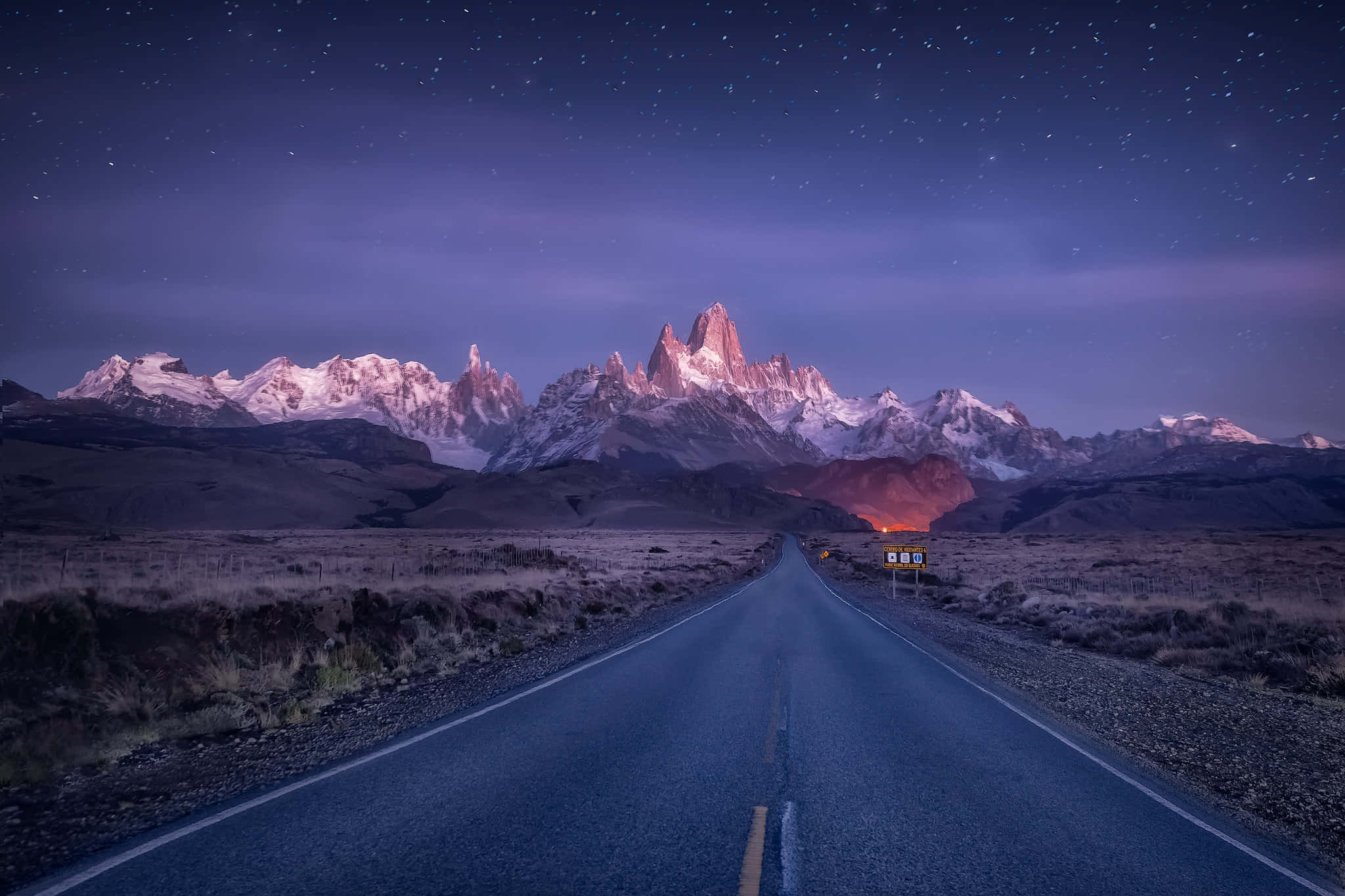 發現巴塔哥尼亞的美景 壁紙 — 星空下的夜空照亮了積雪的山脈，一條孤獨的道路延伸向山峰。