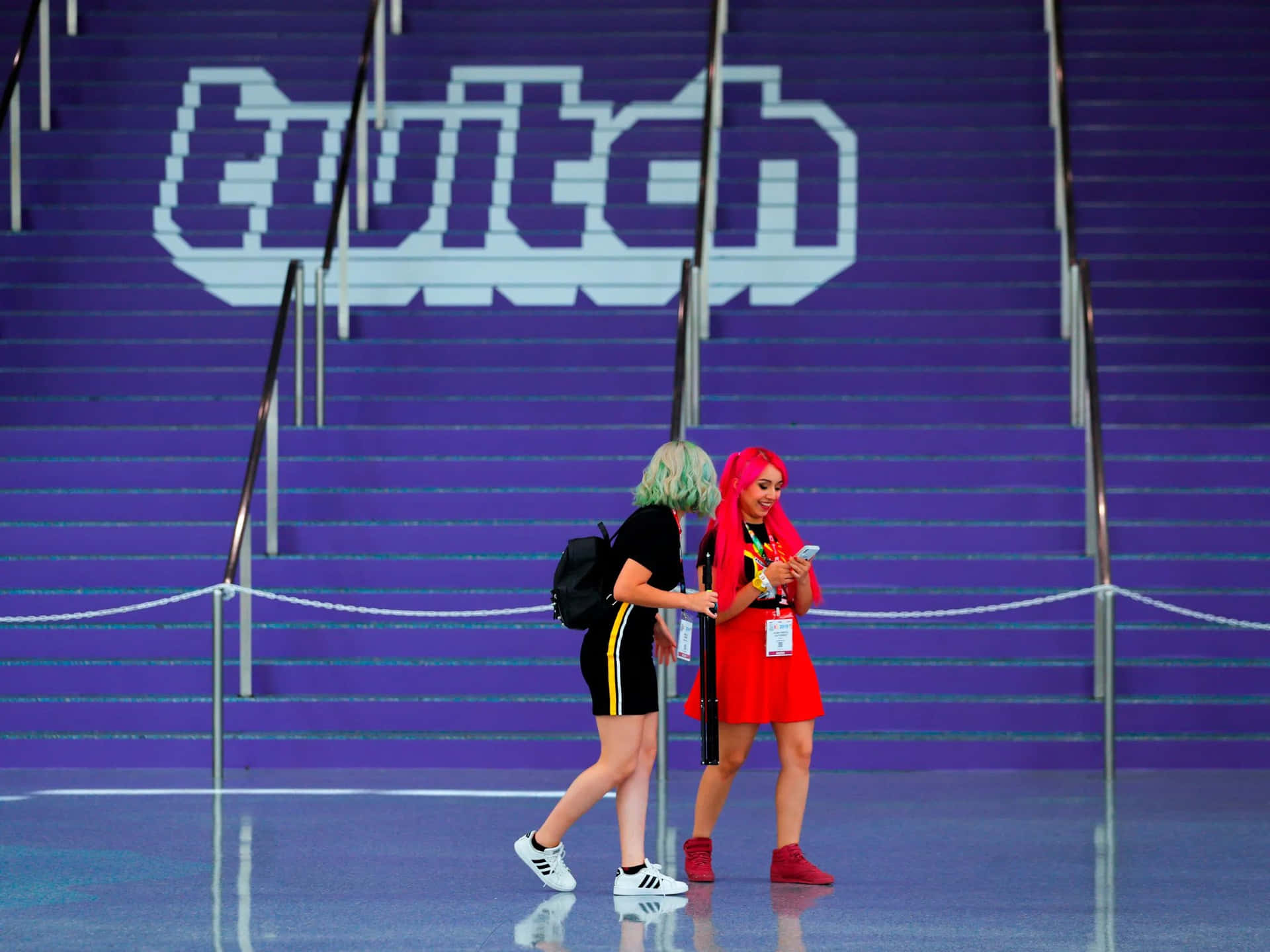 兩位頭髮色彩繽紛的人在會議上走近一個大型Twitch標誌。