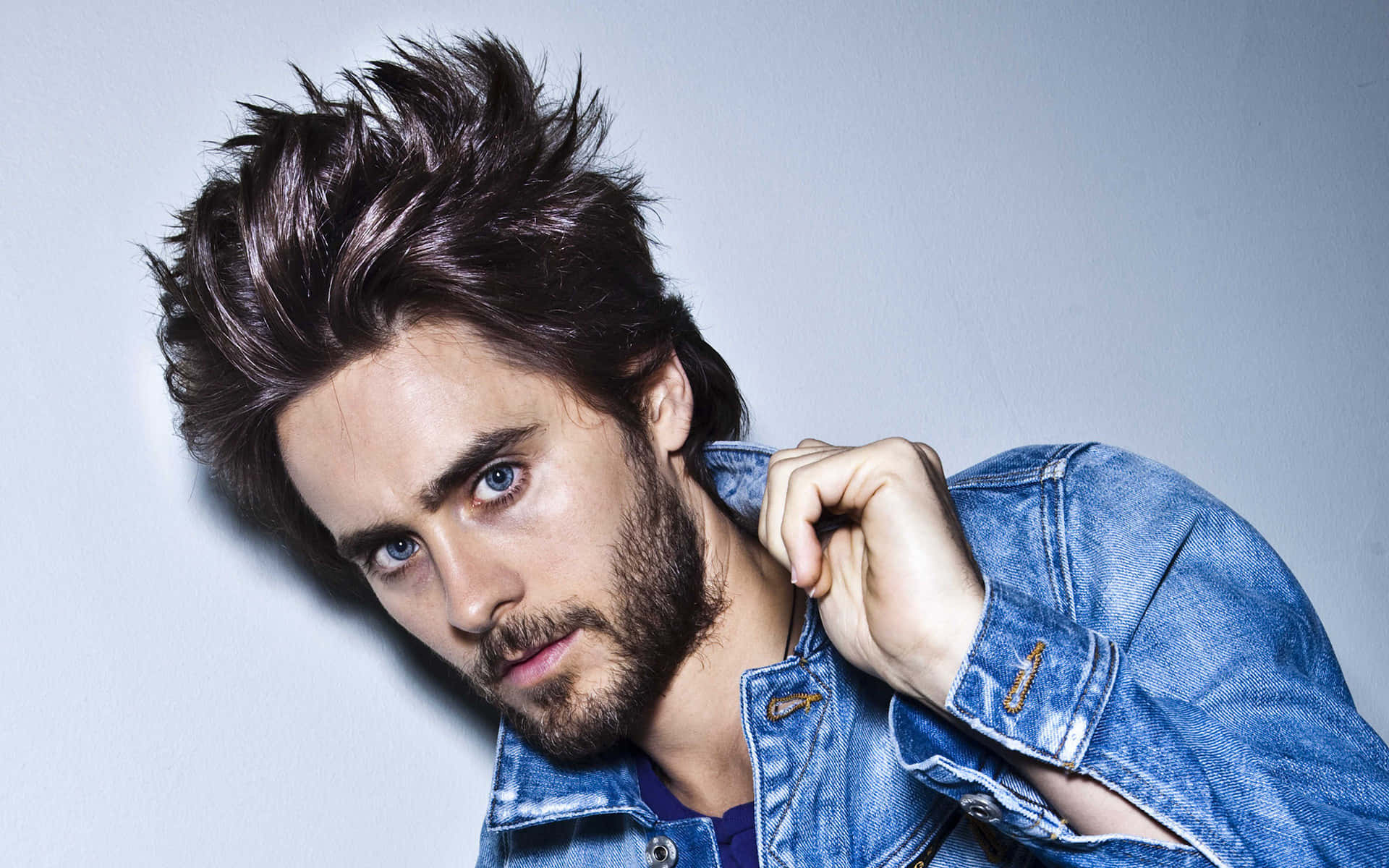 一個擁有尖刺頭髮和鬍鬚的男人，穿著牛仔外套，強烈地看著鏡頭。
