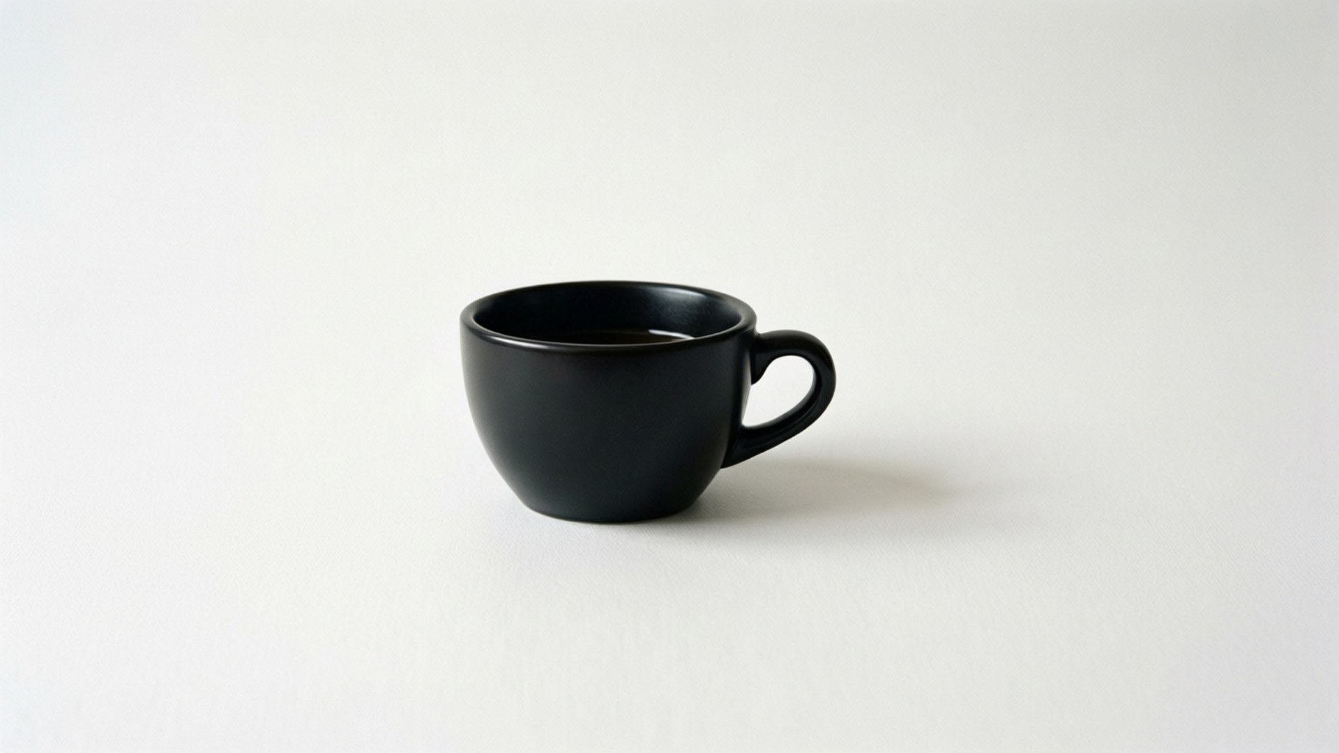 白咖啡杯 壁紙 — 一個時尚的霧面黑色咖啡杯放在明亮的白色表面上，投射出柔和的陰影。