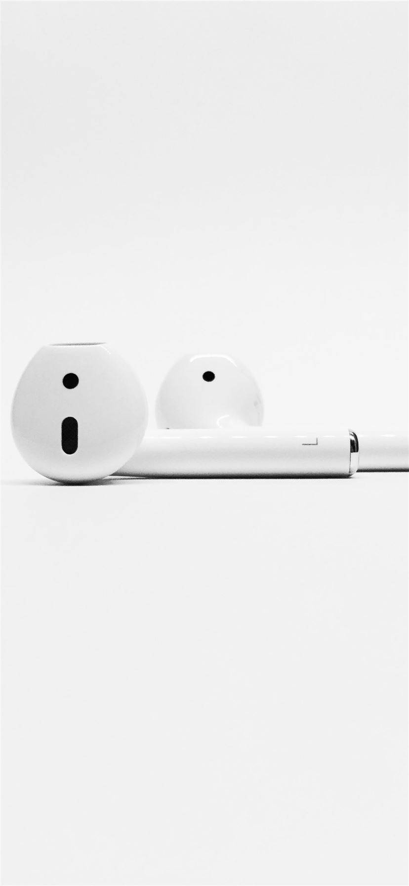 白底 AirPods iPhone 壁紙 — 極簡白色耳機，設計時尚，在柔和燈光下置於純白表面上。