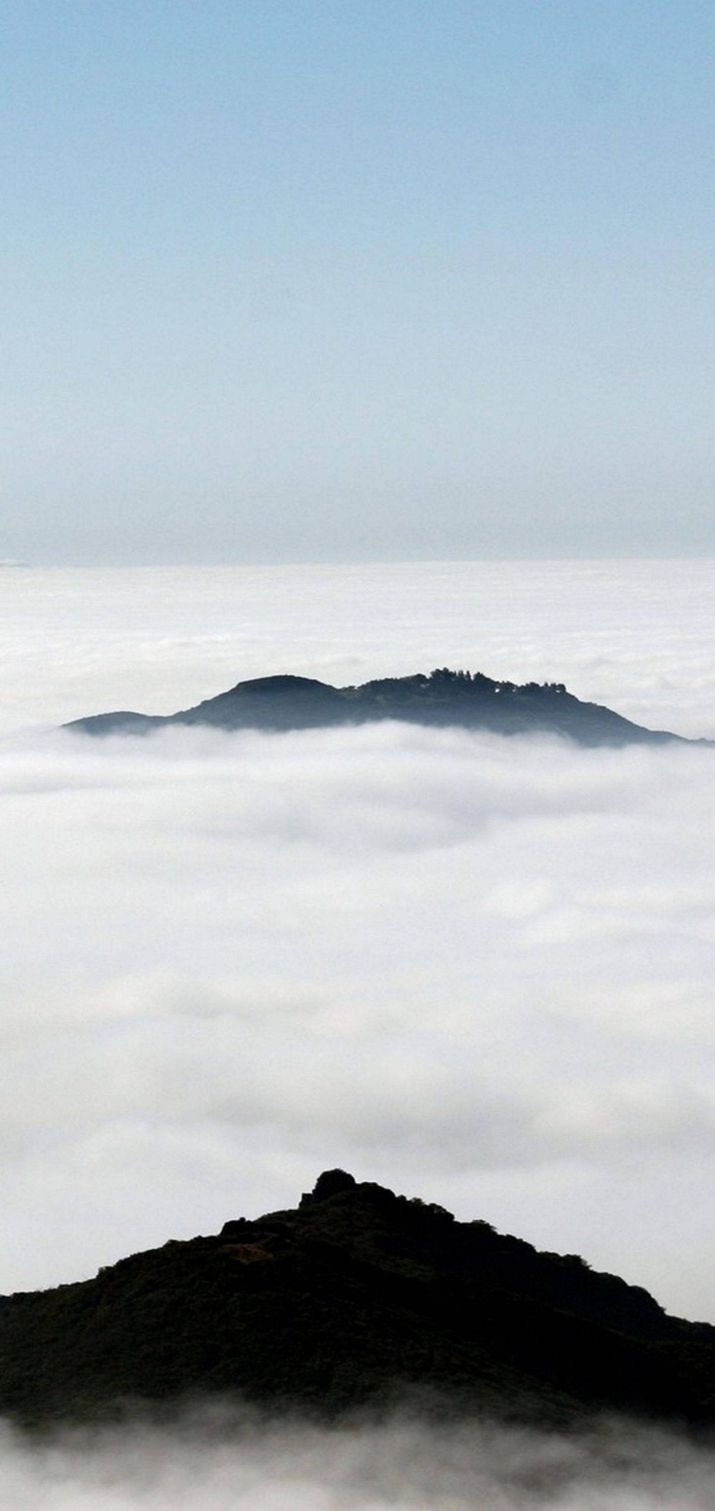 白底iPhone山巒雲霧 壁紙 — 山峰聳立於雲海之上，上方是清澈的藍天。