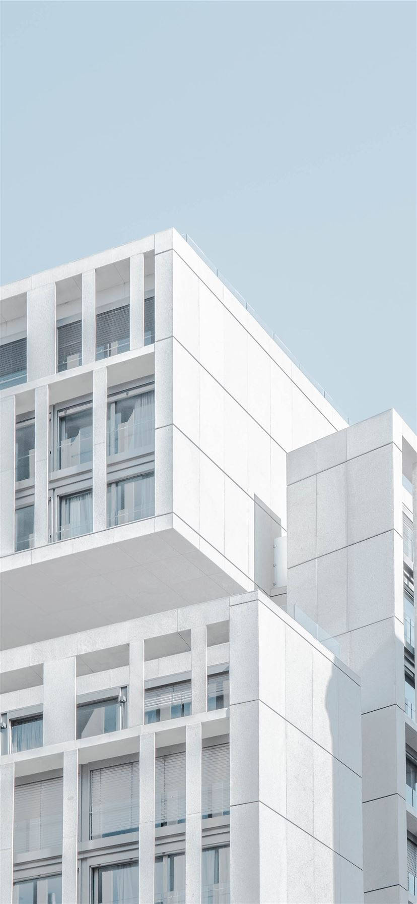白底iPhone現代建築 壁紙 — 現代白色公寓大樓，幾何陽台，清澈淡藍天空下。