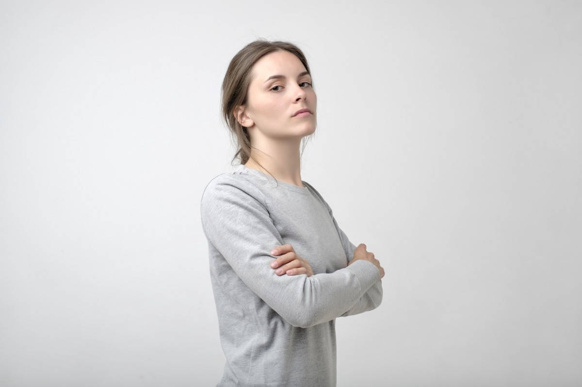 身穿灰色運動衫的女性，雙臂交叉，在攝影棚中看向別處。