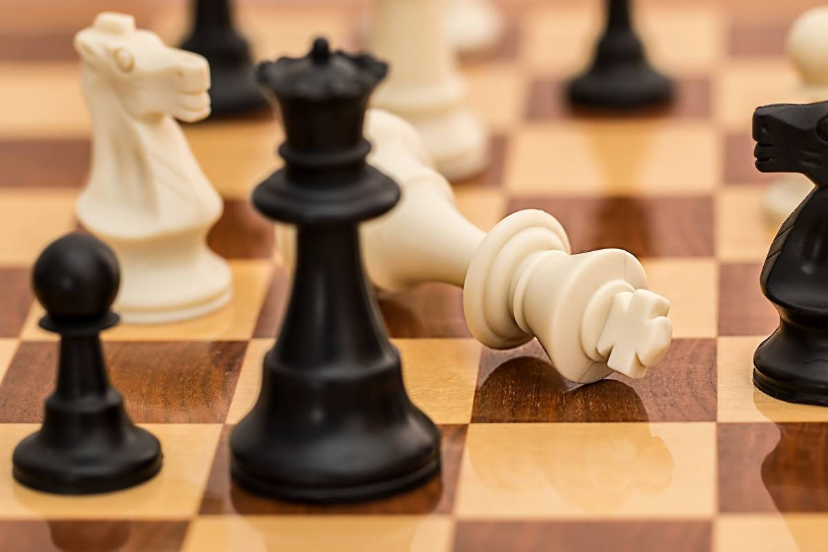 白方棋王受將：戰略與緊張的瞬間 壁紙 — 拋光木方格上棋盤的特寫，顯示倒下的白王和站立的黑棋。