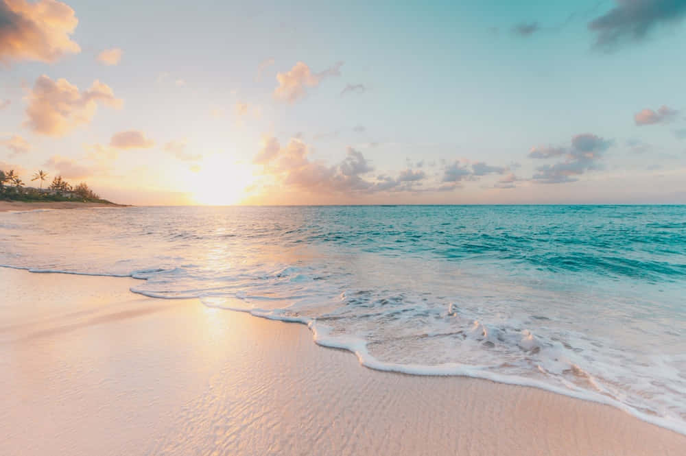 白沙海灘美學夕陽圖片 壁紙 — 夕陽將天空染成柔和的粉紅色和金色，溫柔的海浪在寧靜的熱帶地平線下親吻著沙灘。