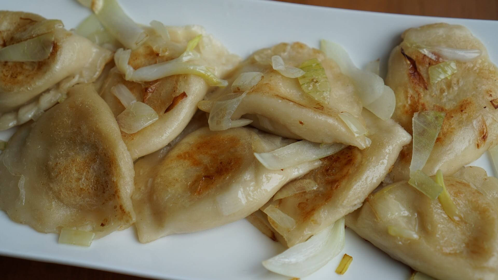 白洋蔥煎波蘭餃子 壁紙 — 金黃色的波蘭餃子配上焦糖洋蔥，在暖光下於白色碟子上閃閃發光。