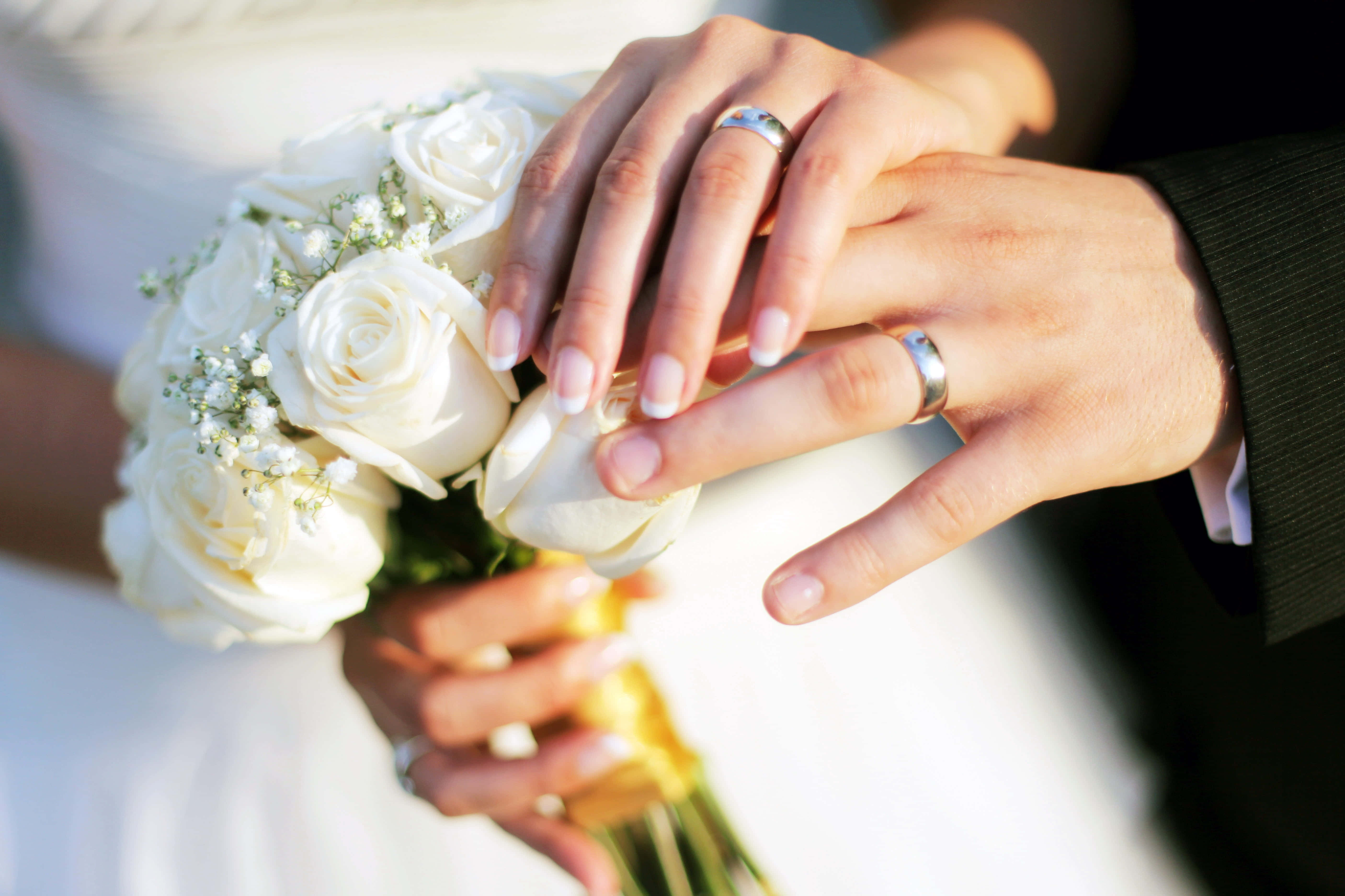 白玫瑰與婚戒的新婚夫婦 壁紙 — 交織的婚禮手部特寫，手持一束白玫瑰，戒指清晰可見。