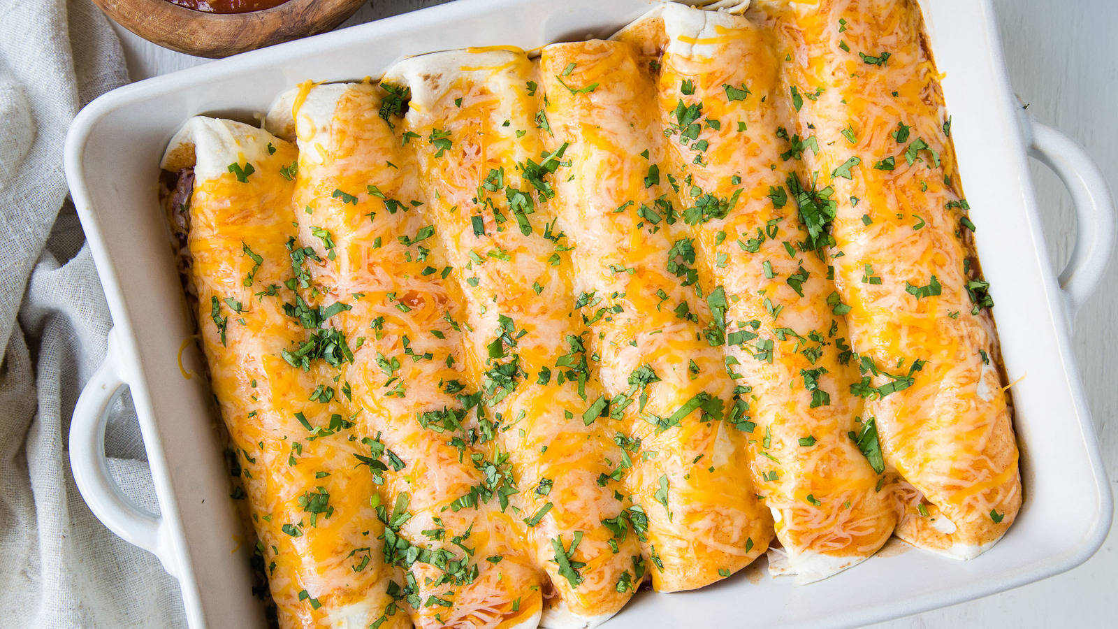 白盤烘烤 enchiladas 壁紙 — 金黃芝士焗玉米餅，飾以新鮮芫荽，置於白色陶瓷烤盤中。