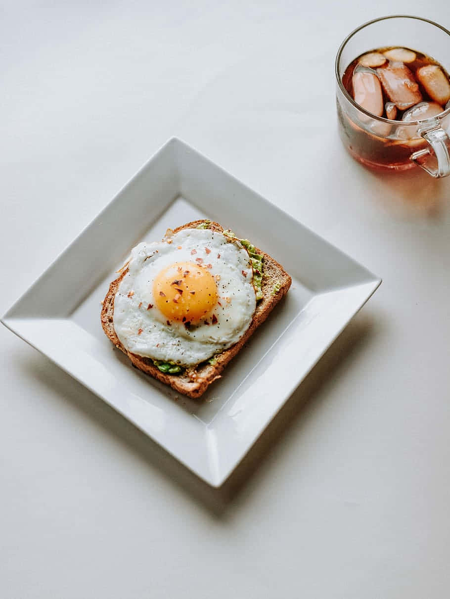 Egg White 桌布 壁紙 — 白碟上嘅牛油果多士上面有太陽蛋，旁邊有杯冰茶。