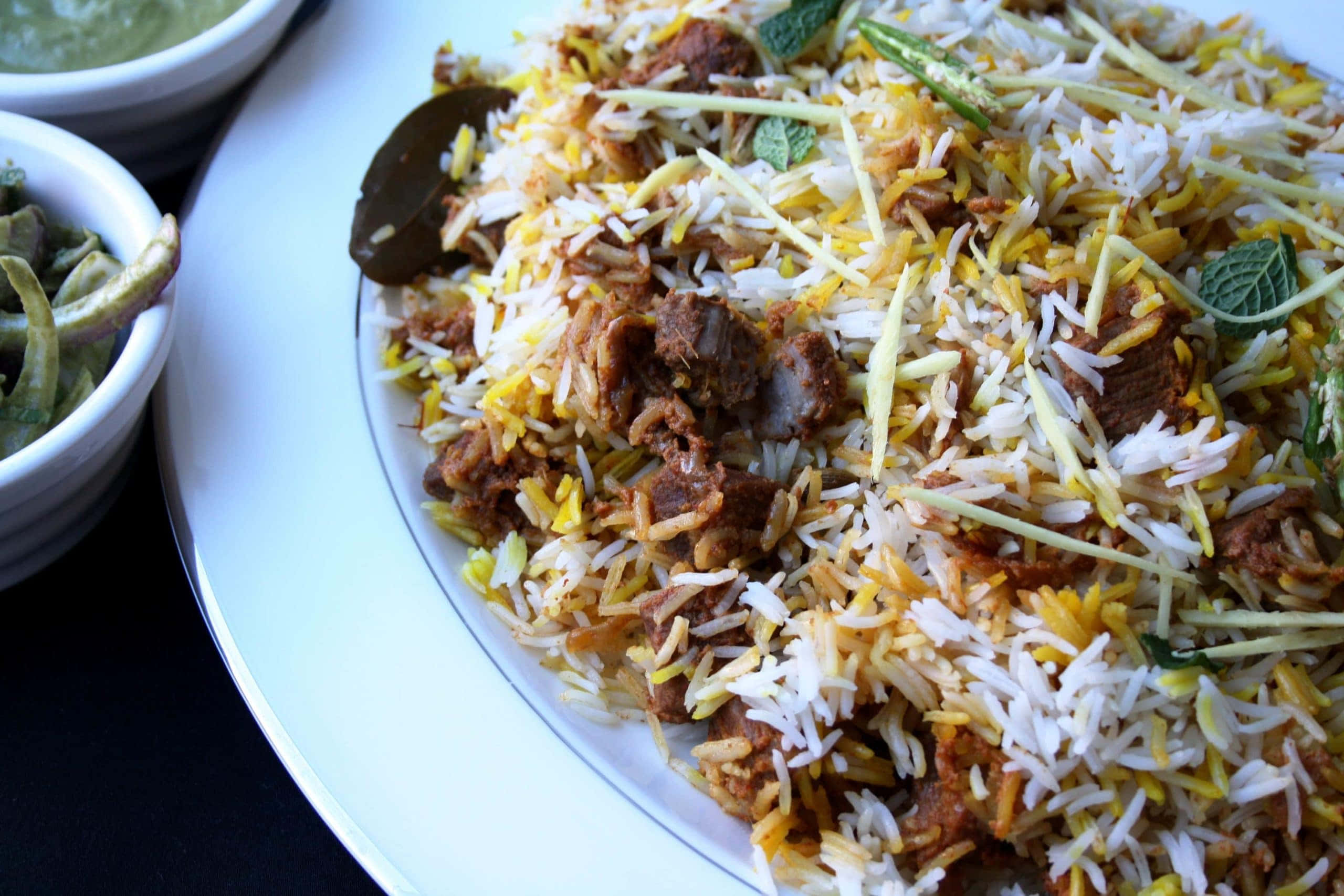 Biryani 桌布 壁紙 — 白碟上香氣撲鼻的印度香飯特寫，配有嫩肉、黃飯、薄荷和切片薑裝飾。