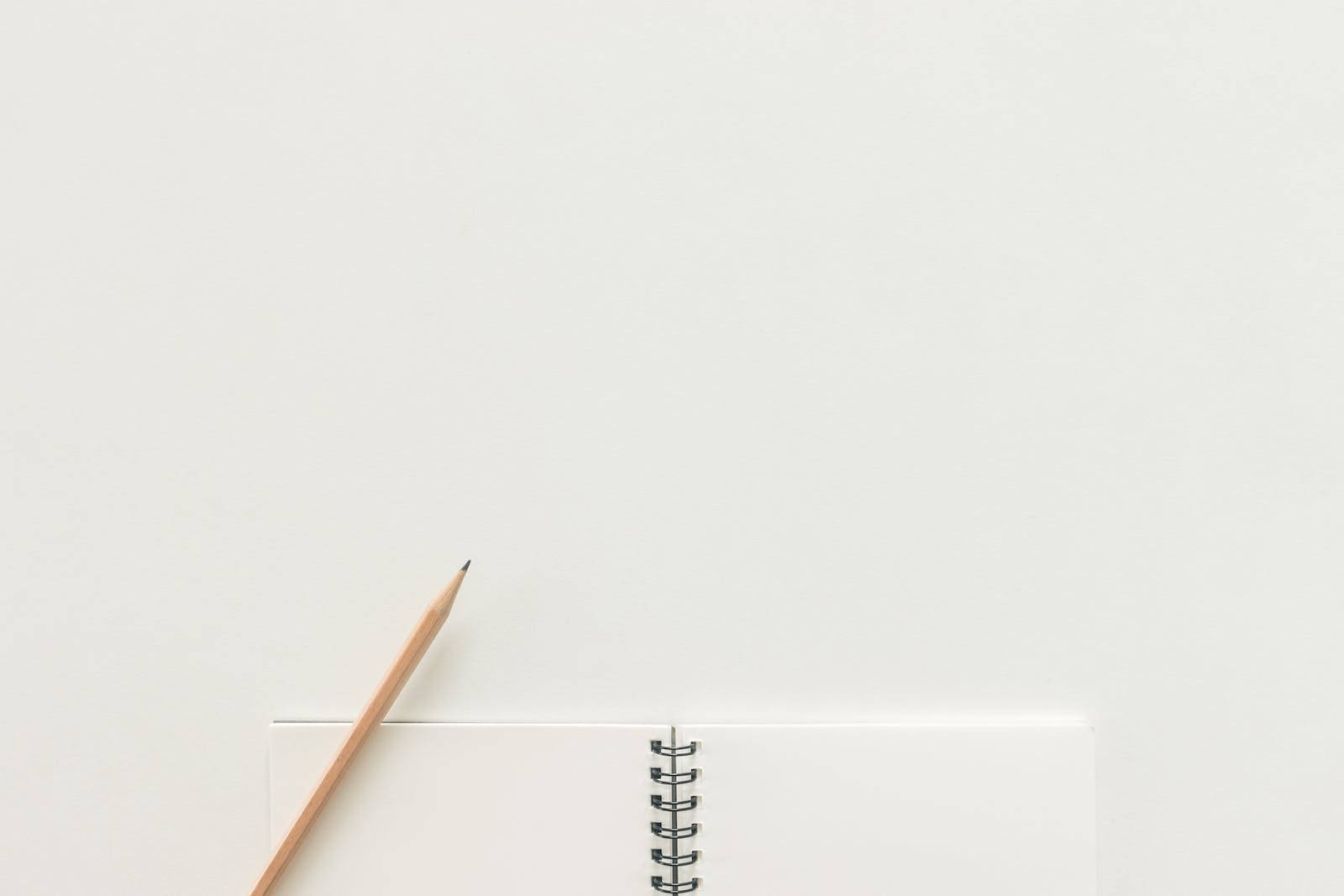 白紙紋理筆記本與鉛筆 壁紙 — 一個極簡風格的俯視圖，顯示一支木鉛筆放在一個打開的螺旋筆記本旁邊，背景是純白色表面。