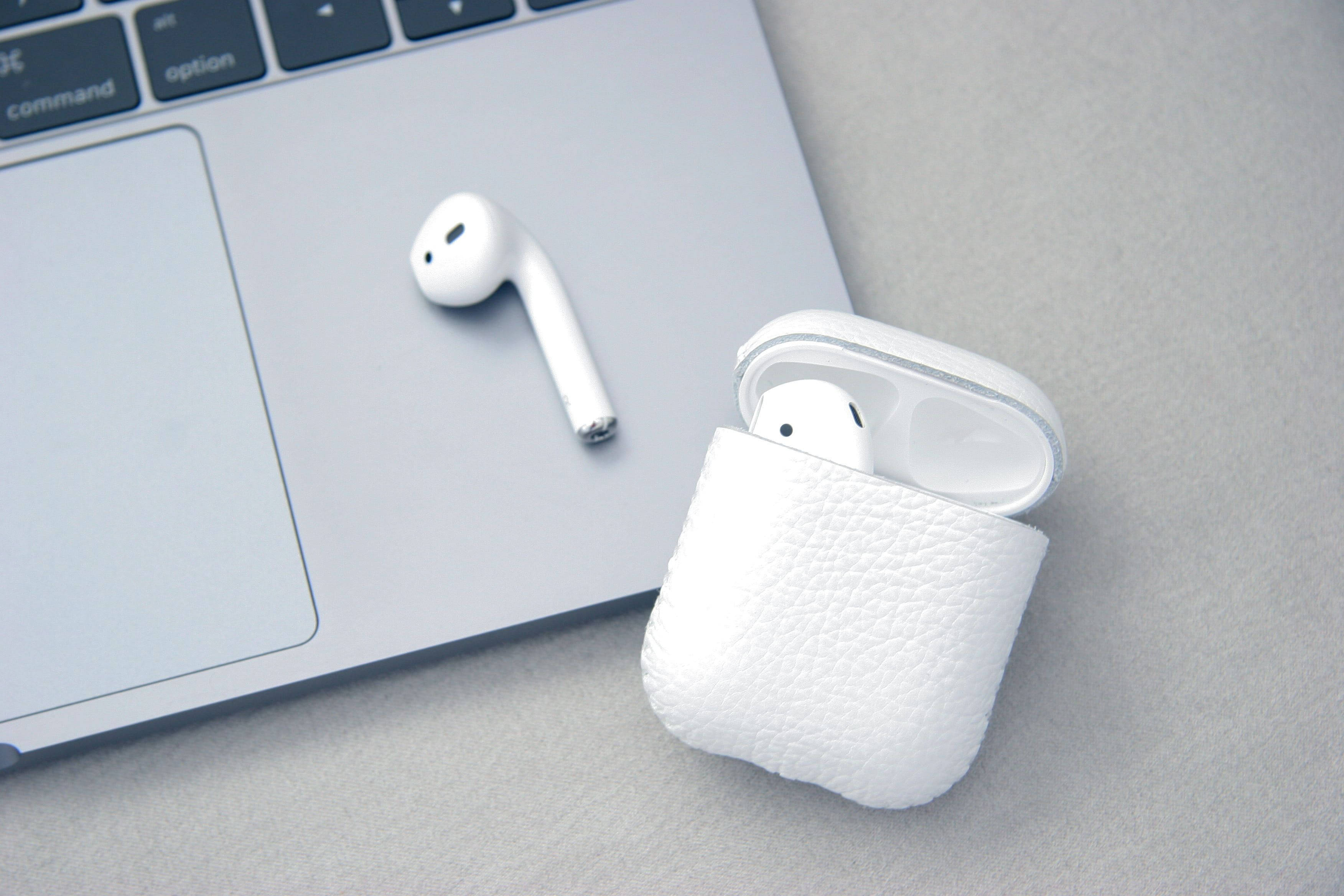 白色 AirPods 與 MacBook 壁紙 — 一個白色無線耳塞放在其紋理充電盒旁邊，置於時尚的筆記型電腦鍵盤上。