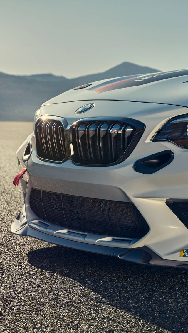 白色BMW M2賽車在沙漠碎石路上的正面視圖，背景有山脈和日落。