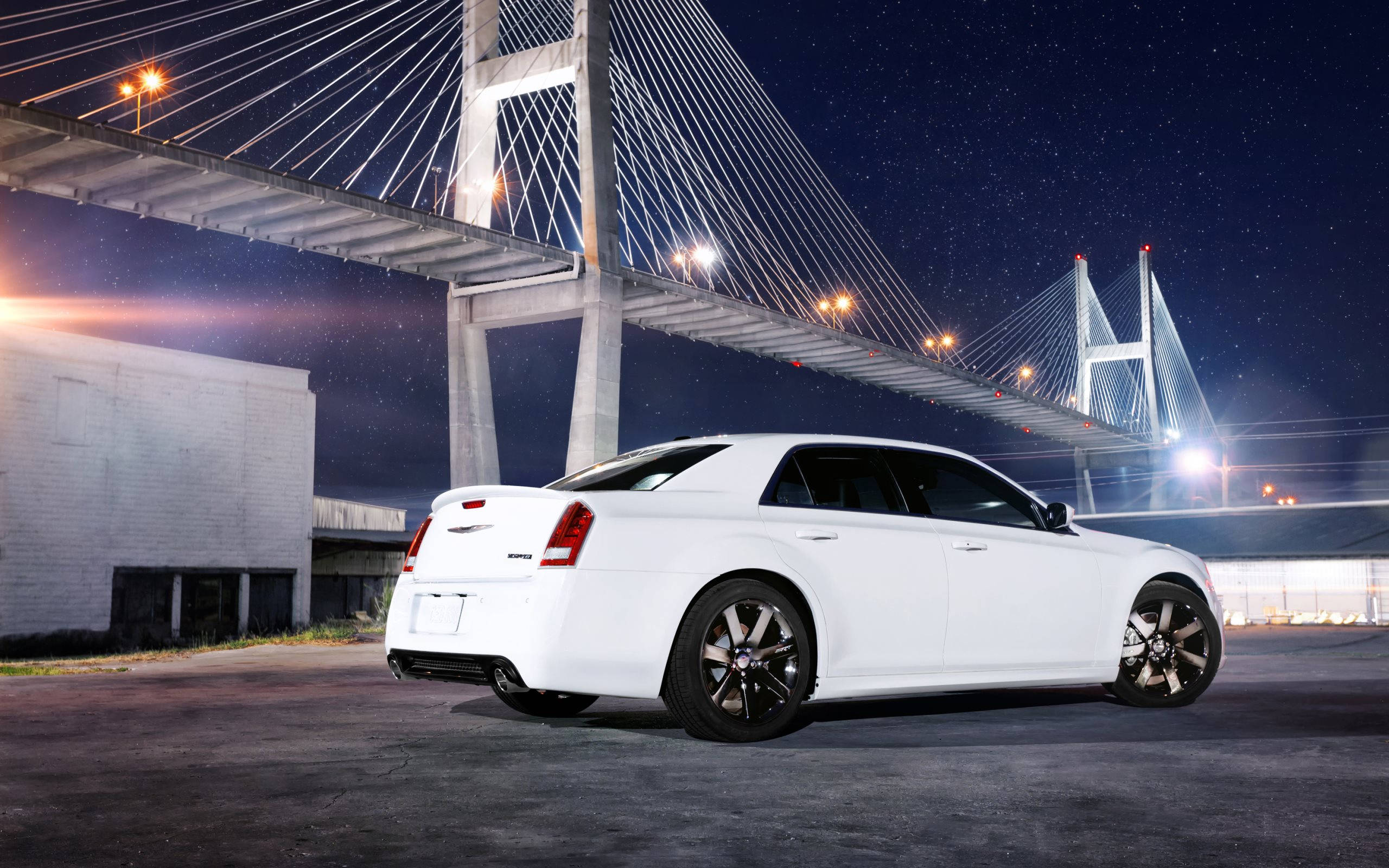 白色 Chrysler 300 SRT 壁紙 — 一輛時尚的白色轎車停泊在燈光璀璨的吊橋下，背景是滿天繁星的夜空。