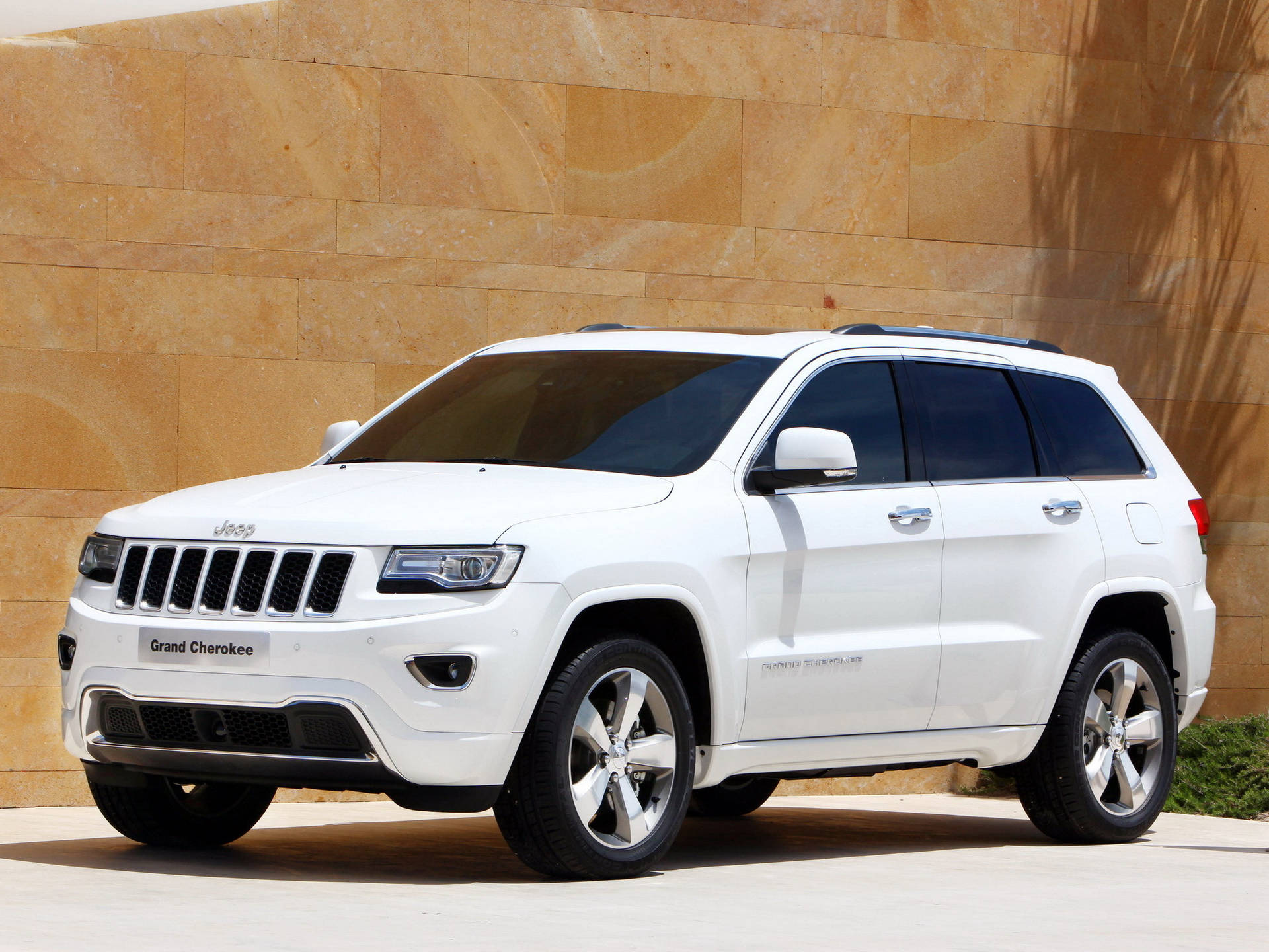 白色Jeep Grand Cherokee在白天停靠在石牆旁。