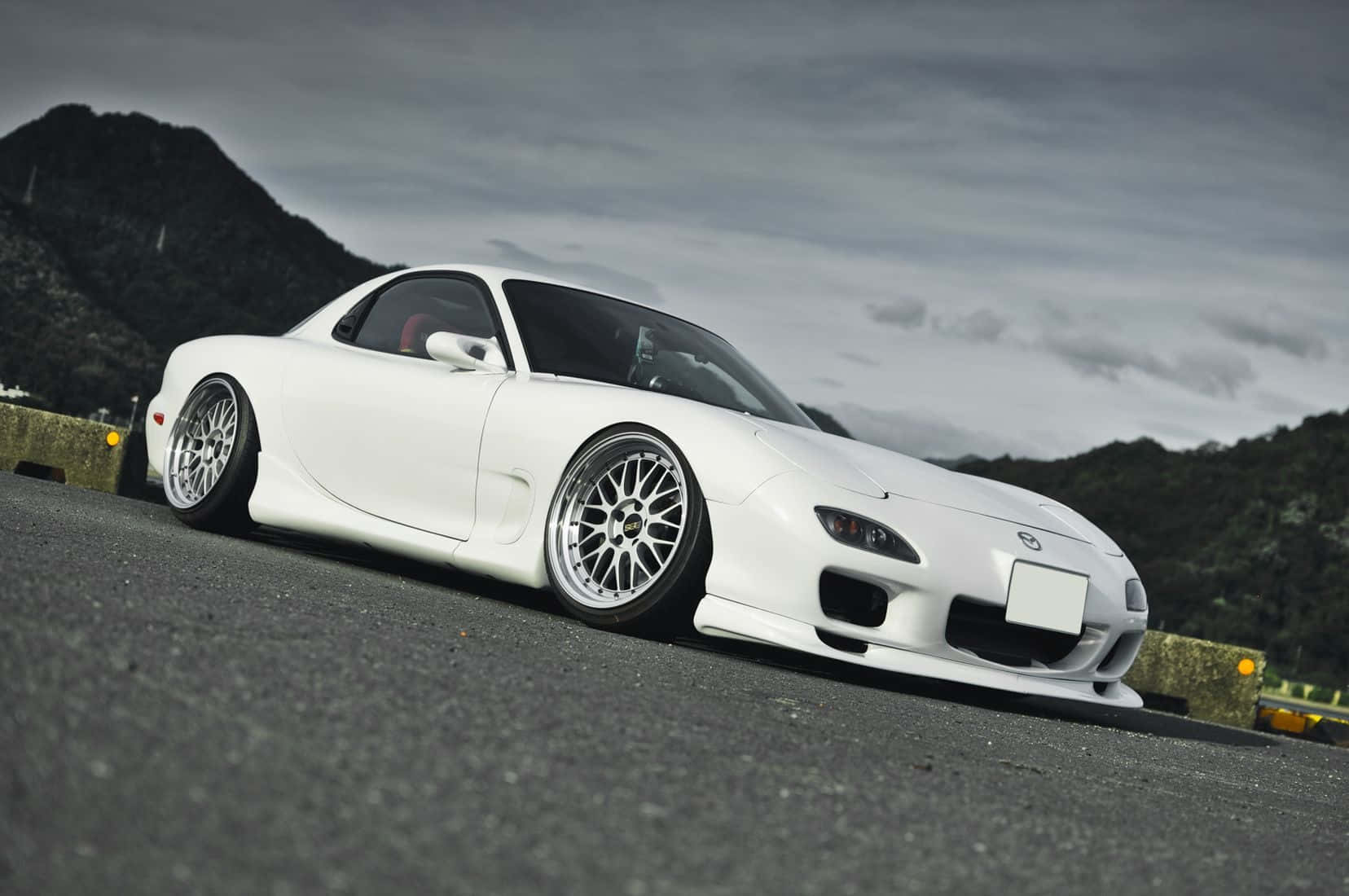 白色萬事得RX-7跑車在山路上，天空多雲