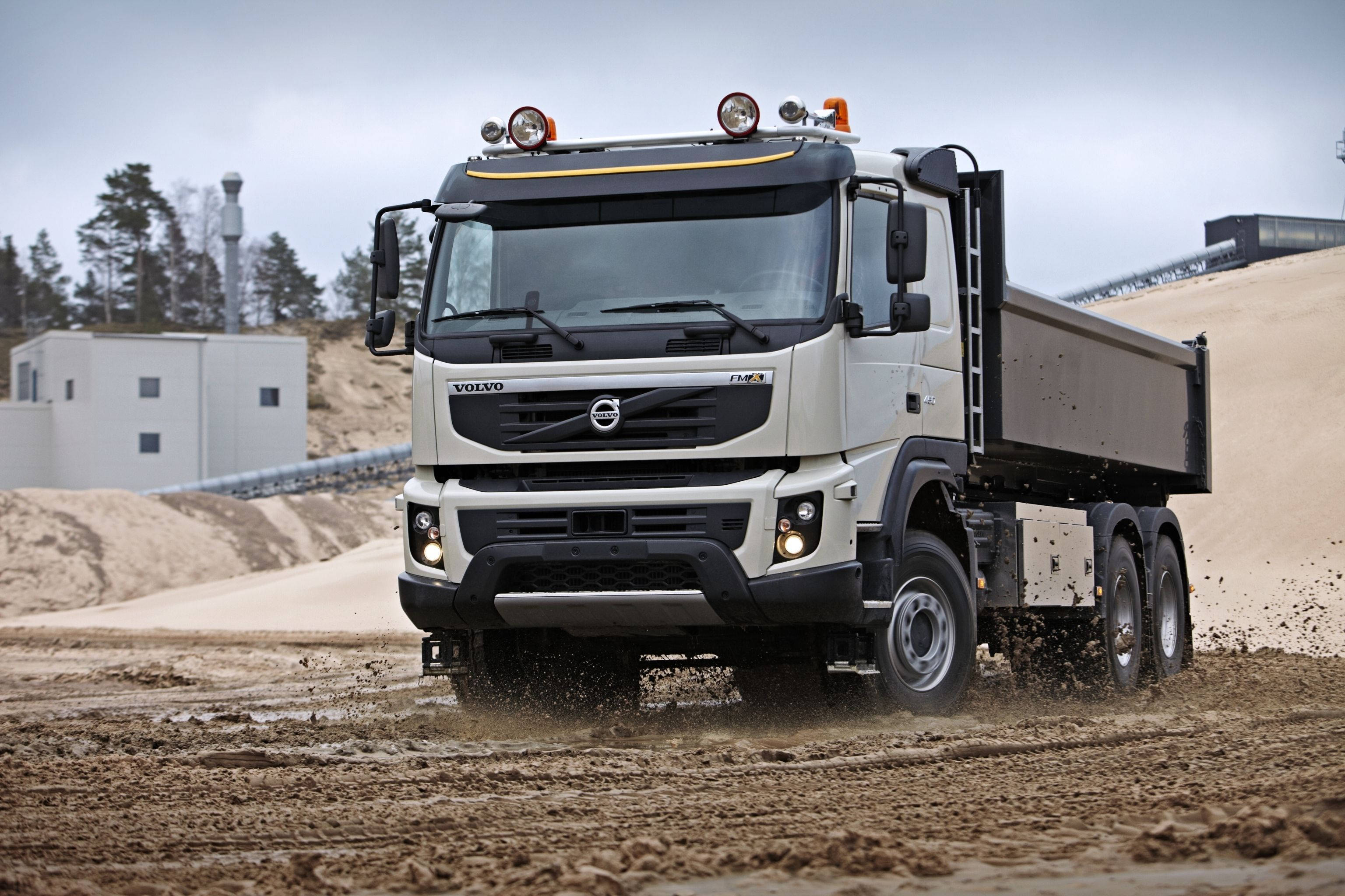 白色 Volvo 冷氣自卸車 壁紙 — 一輛白色富豪自卸車在建築工地的泥濘地形上行駛，在陰天揚起泥土。