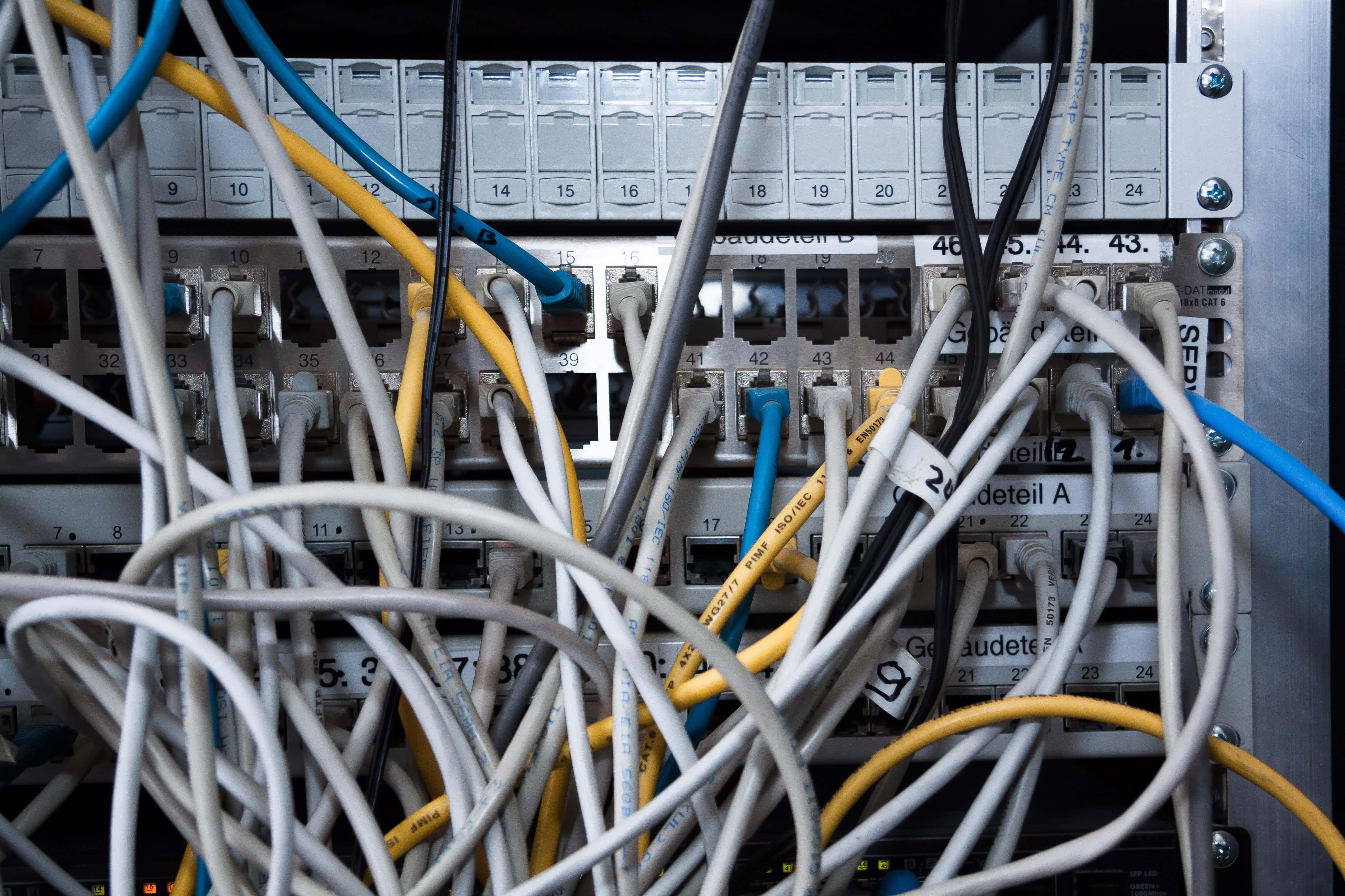 Ethernet 桌布 壁紙 — 白色、黃色和藍色網絡電纜混亂纏結，插入伺服器機架端口面板。