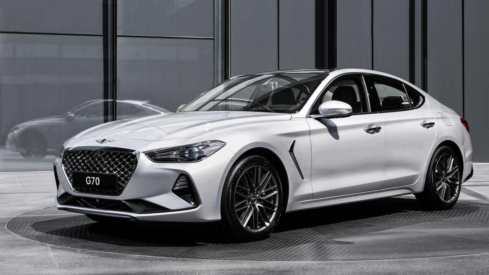 白色現代 G70 轎車在現代玻璃展廳中展示，帶有倒影。