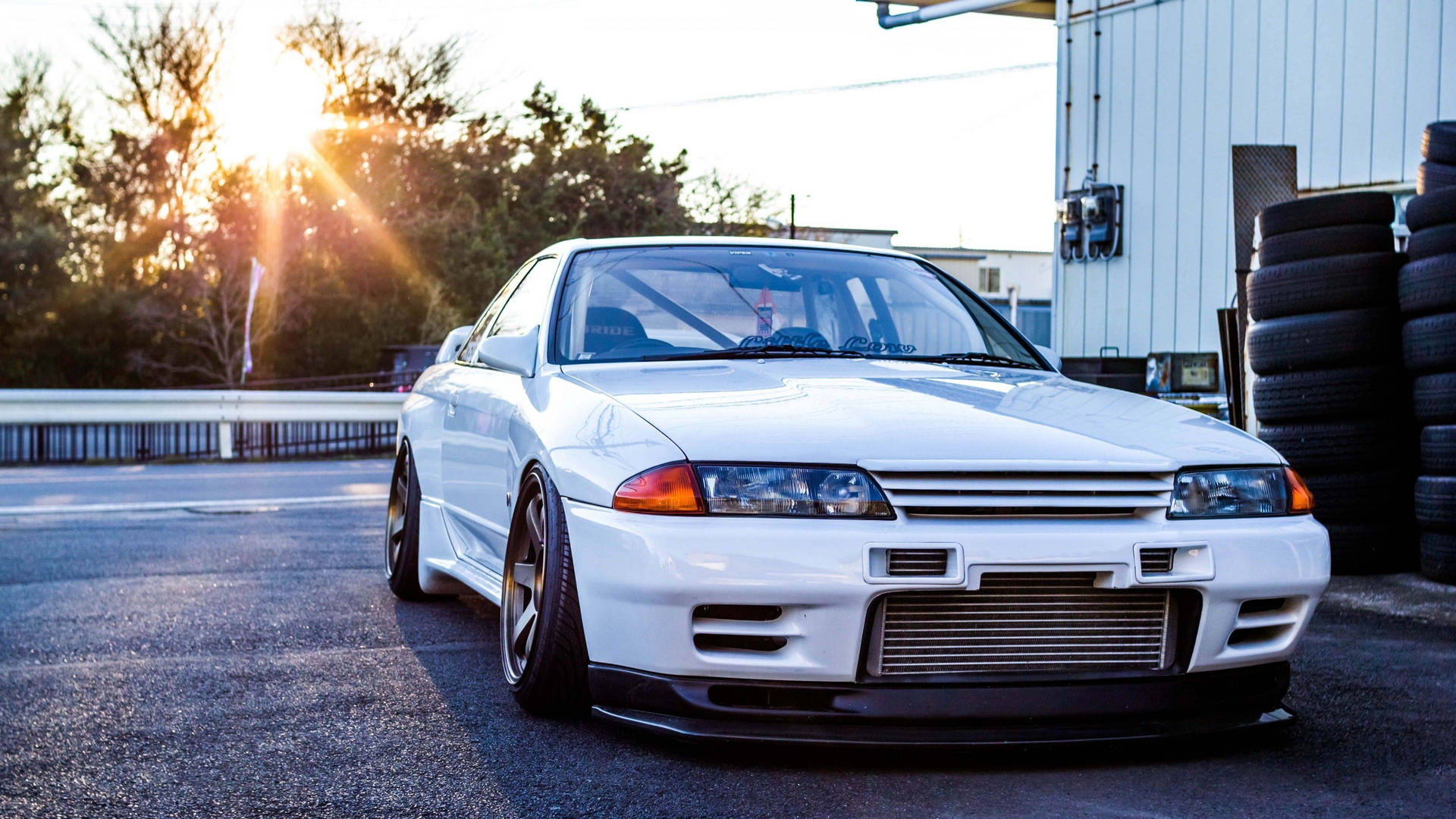 白色日產Skyline GT-R在日落時停泊在堆疊輪胎附近。